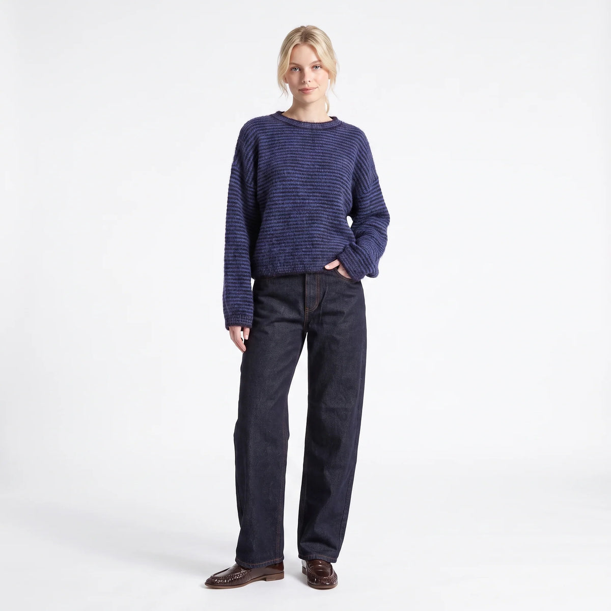 A woman modeling a navy blue textured knit sweater and dark indigo jeans against a clean white studio background.