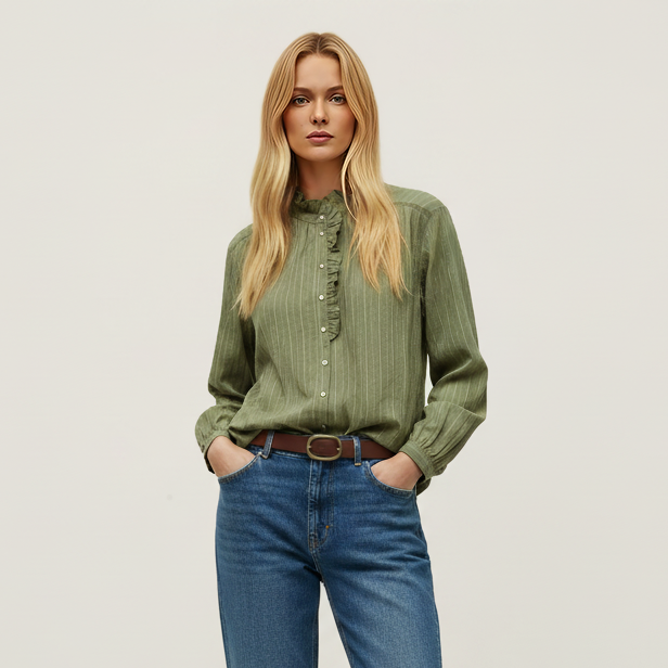 A woman modeling a sage green button-up shirt with vertical texture, tucked into blue jeans with a brown belt, and wearing tan suede shoes, against a plain light gray studio background.