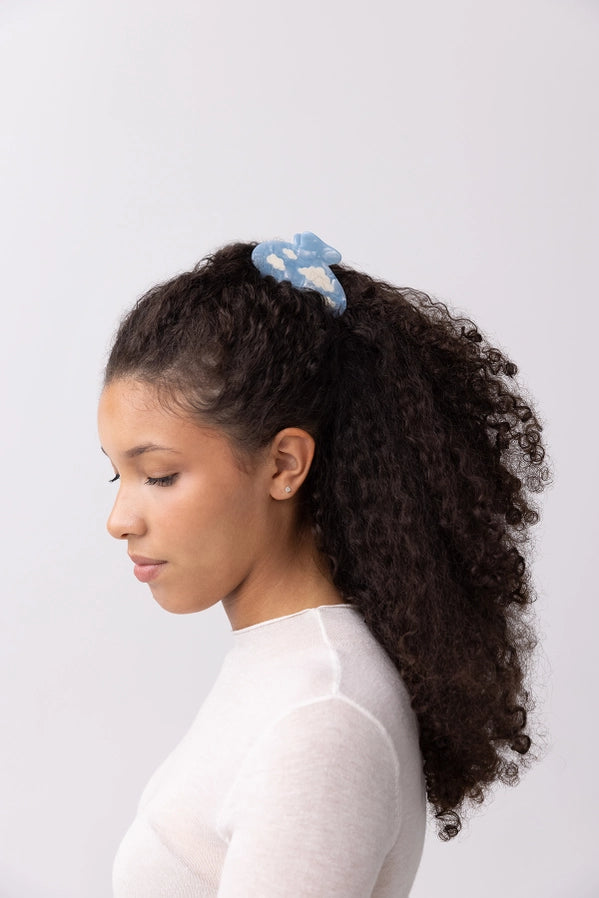 Woman with curly hair wearing a blue hair accessory against a white background