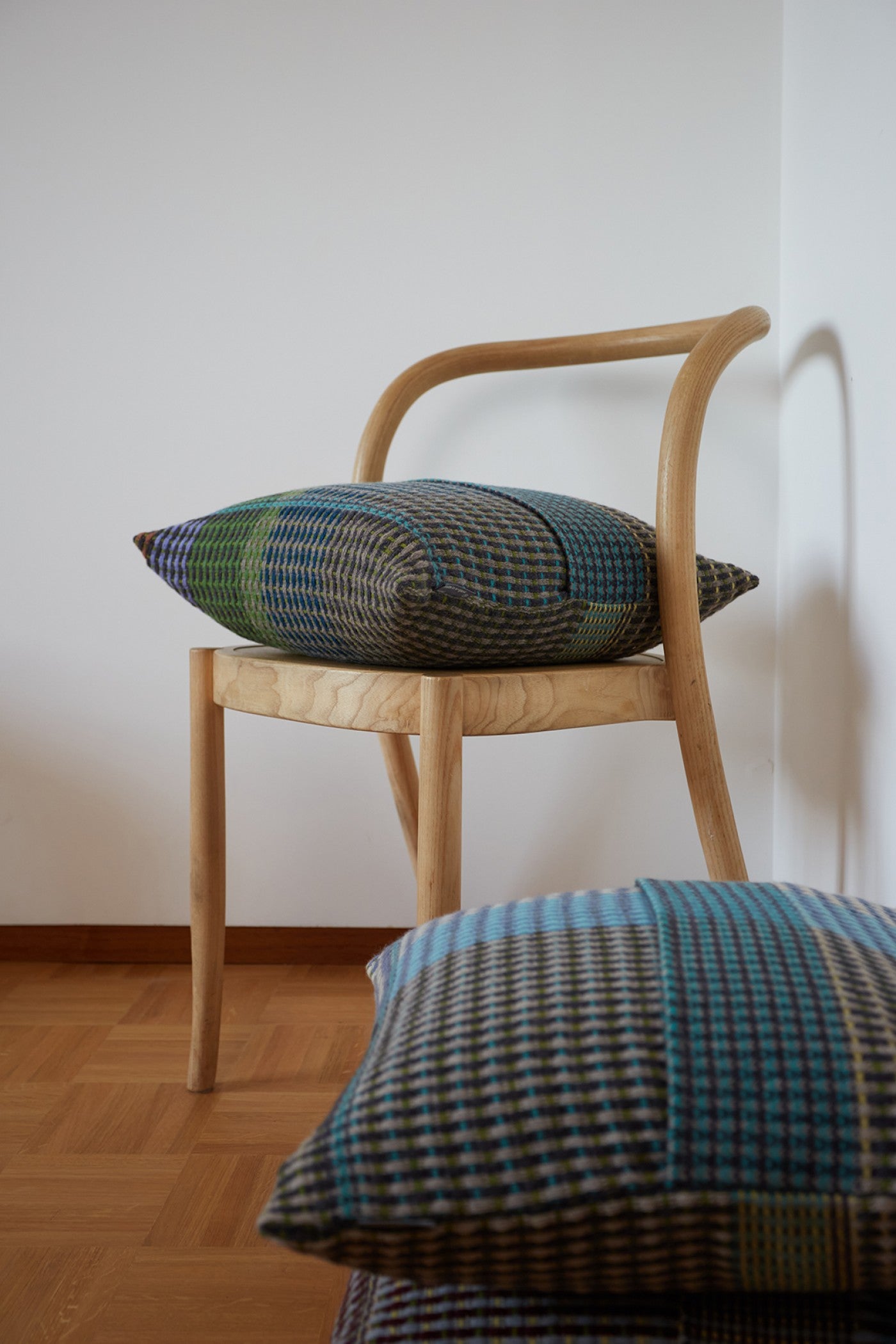 Two patterned wool throw pillows rest on a light wood chair.