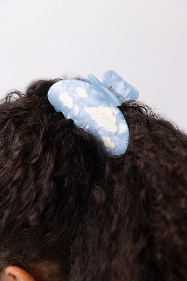 Blue hair clip with cloud design on a person's hair against a white background