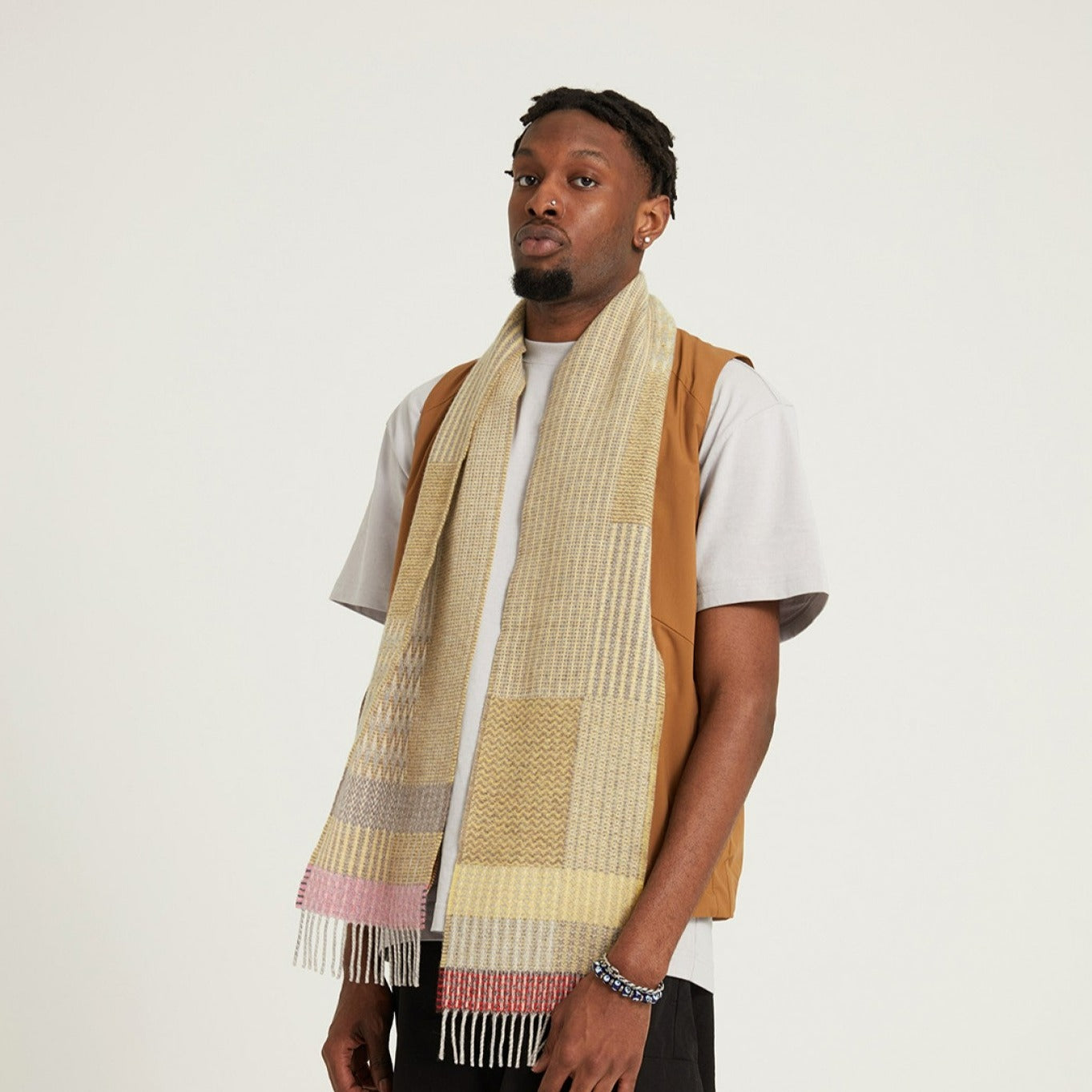A beige and yellow patterned wool scarf with pink and red fringe.