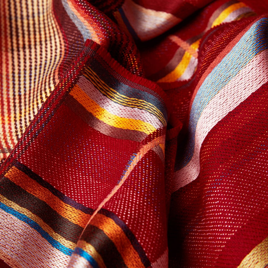 Red woven fabric with multicolored stripes in orange, yellow, blue, and beige.