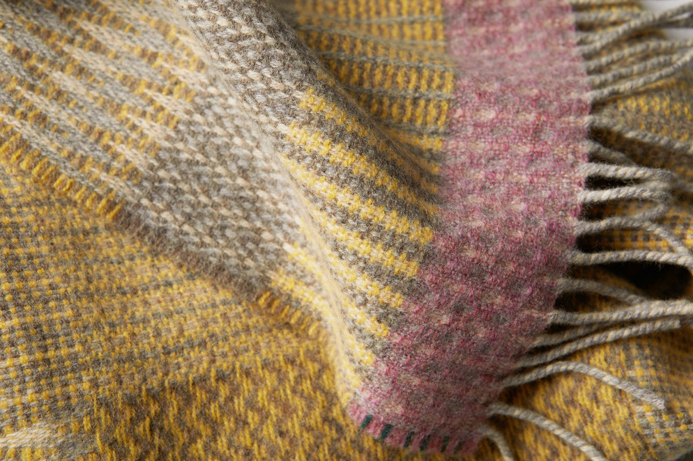 Woven wool scarf in mustard yellow, gray, and mauve plaid pattern with fringed edges.