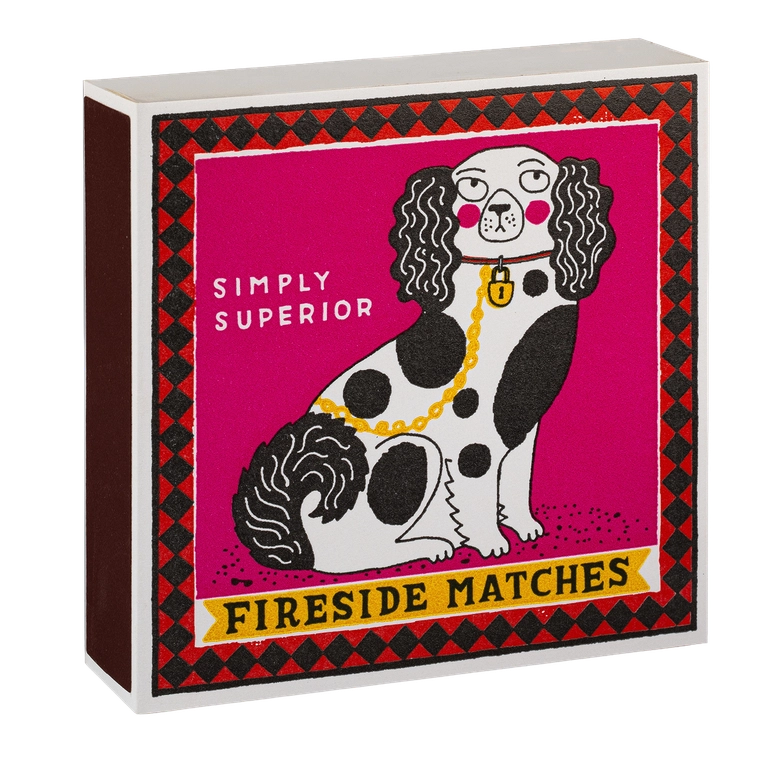 A box of Fireside Matches featuring a vintage-style illustration of a black-and-white spotted dog on a bright pink front panel with a red-and-black diamond border and the words 'SIMPLY SUPERIOR' and 'FIRESIDE MATCHES'.