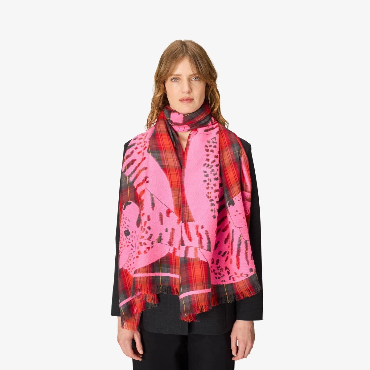 A model wearing a vibrant pink and red patterned scarf with black and white graphic elements, styled over a black jacket against a plain white background.