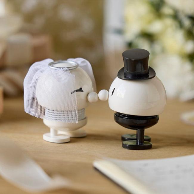 Pair of kissing bride and groom figurines; bride wears a veil, groom a top hat.  They are white with black accents.