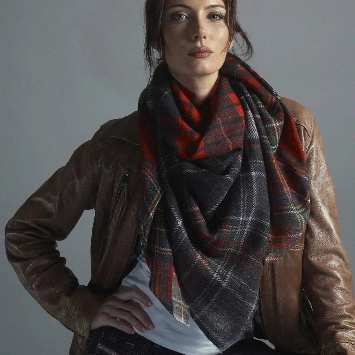 Woman wearing a plaid scarf and brown leather jacket against a gray background