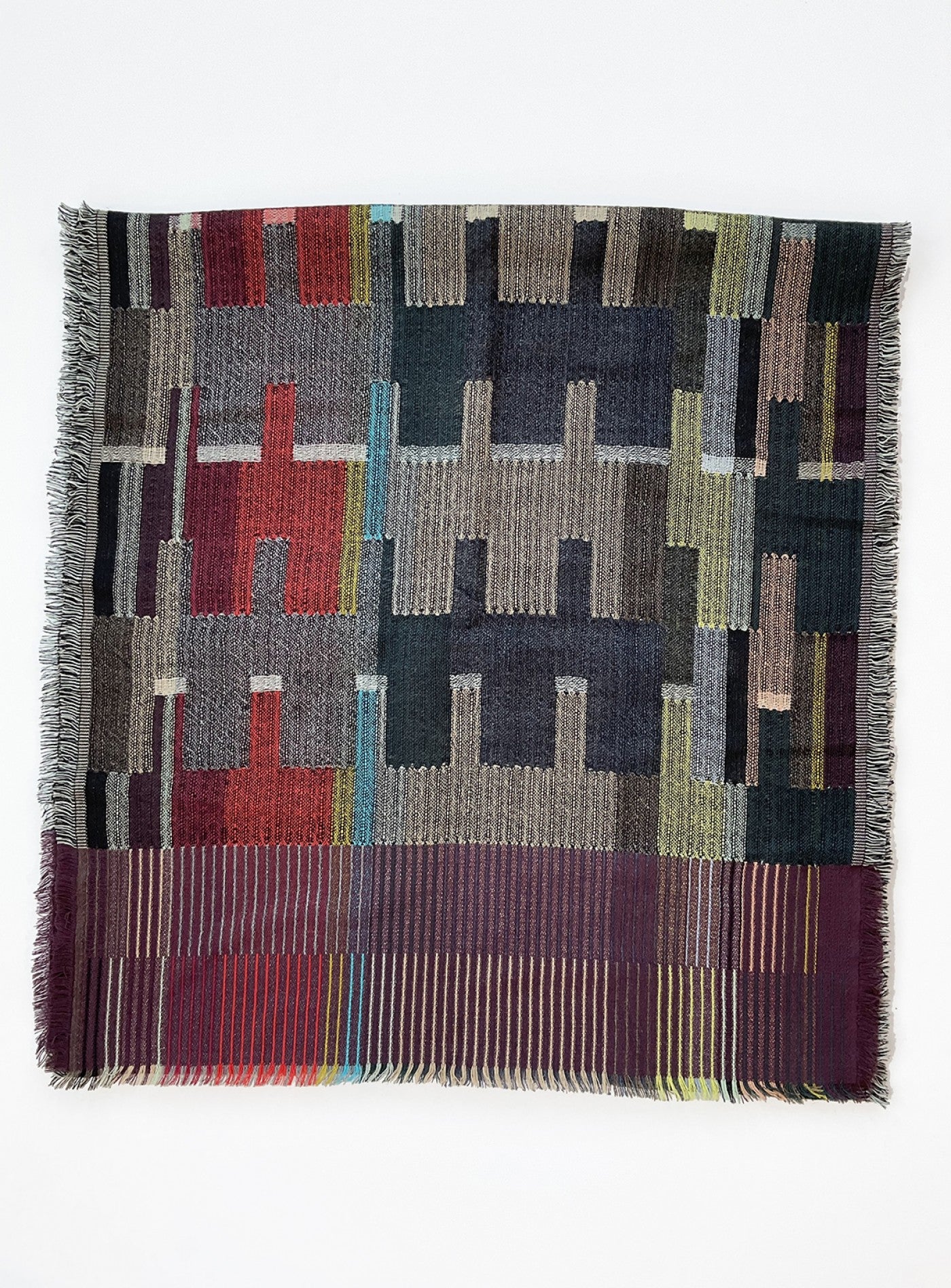 Woven textile with geometric pattern in muted reds, greens, and grays; fringed edges.