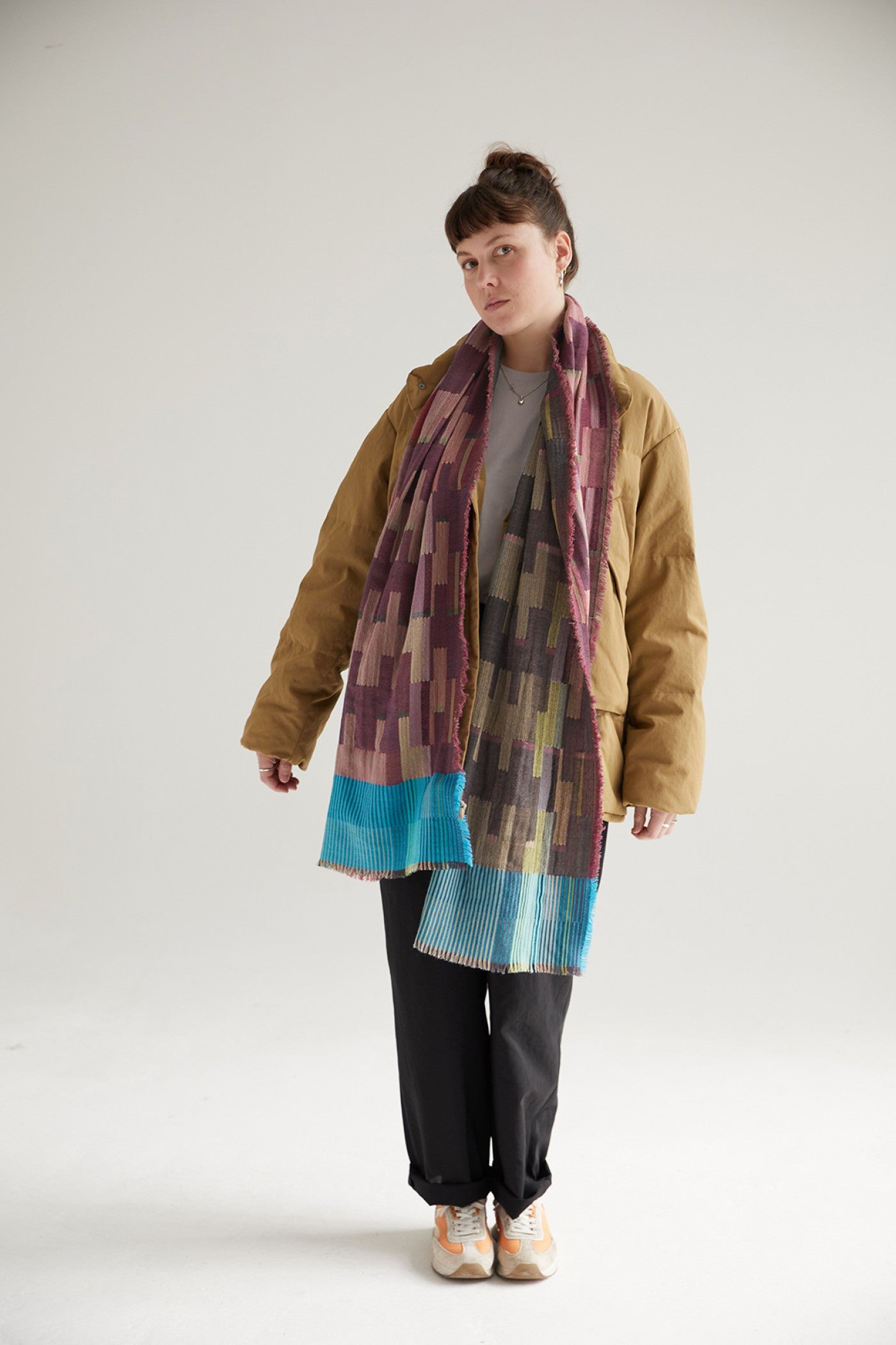 Geometric patterned scarf in purple, green, and teal, with a pleated turquoise border.