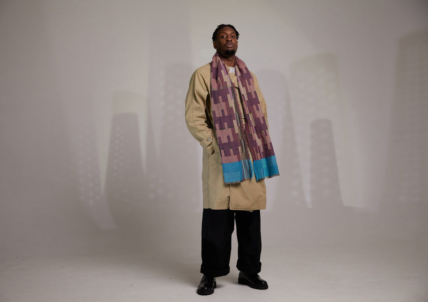 A man wearing a beige trench coat and a purple and teal patterned scarf.