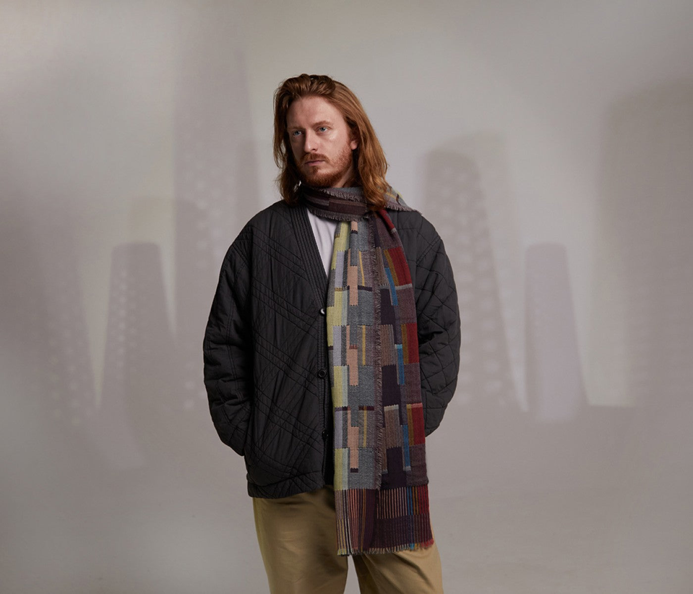 Man wearing a black quilted jacket and a multicolored geometric patterned scarf.