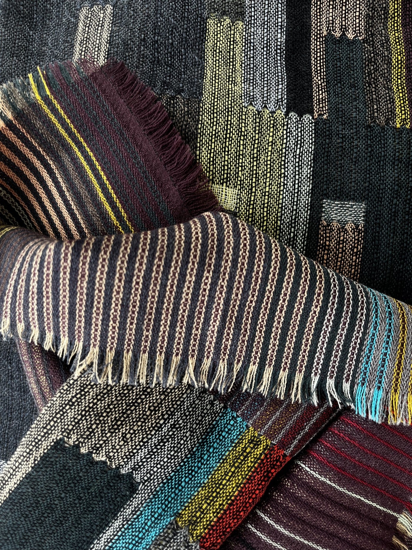Woven scarf with multicolored stripes and textured patterns in dark browns, blacks, and teal.  Fringed edges.