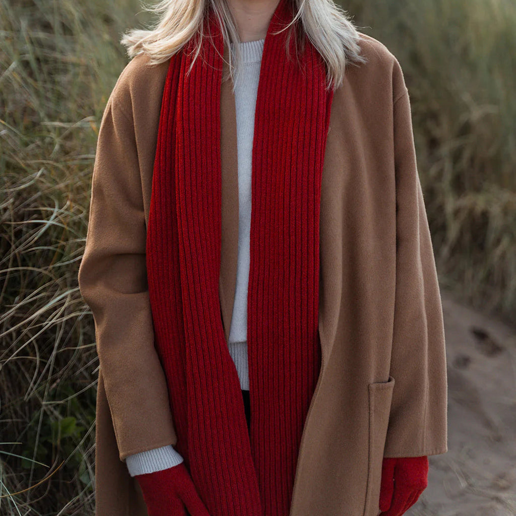 Woman wearing a red beanie, scarf, and gloves standing on a grassy hillside.