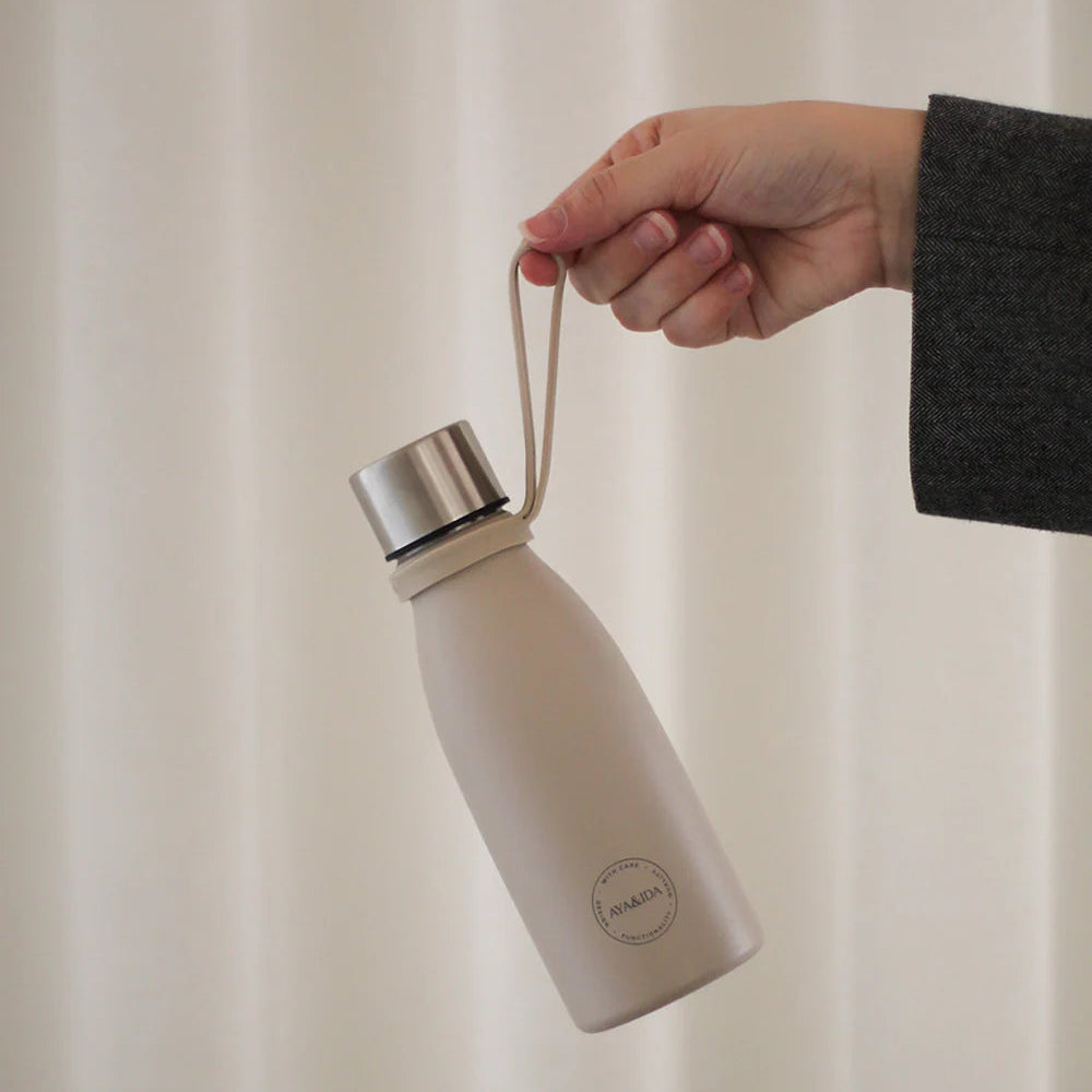 Person holding a beige insulated bottle with a black label against a neutral background