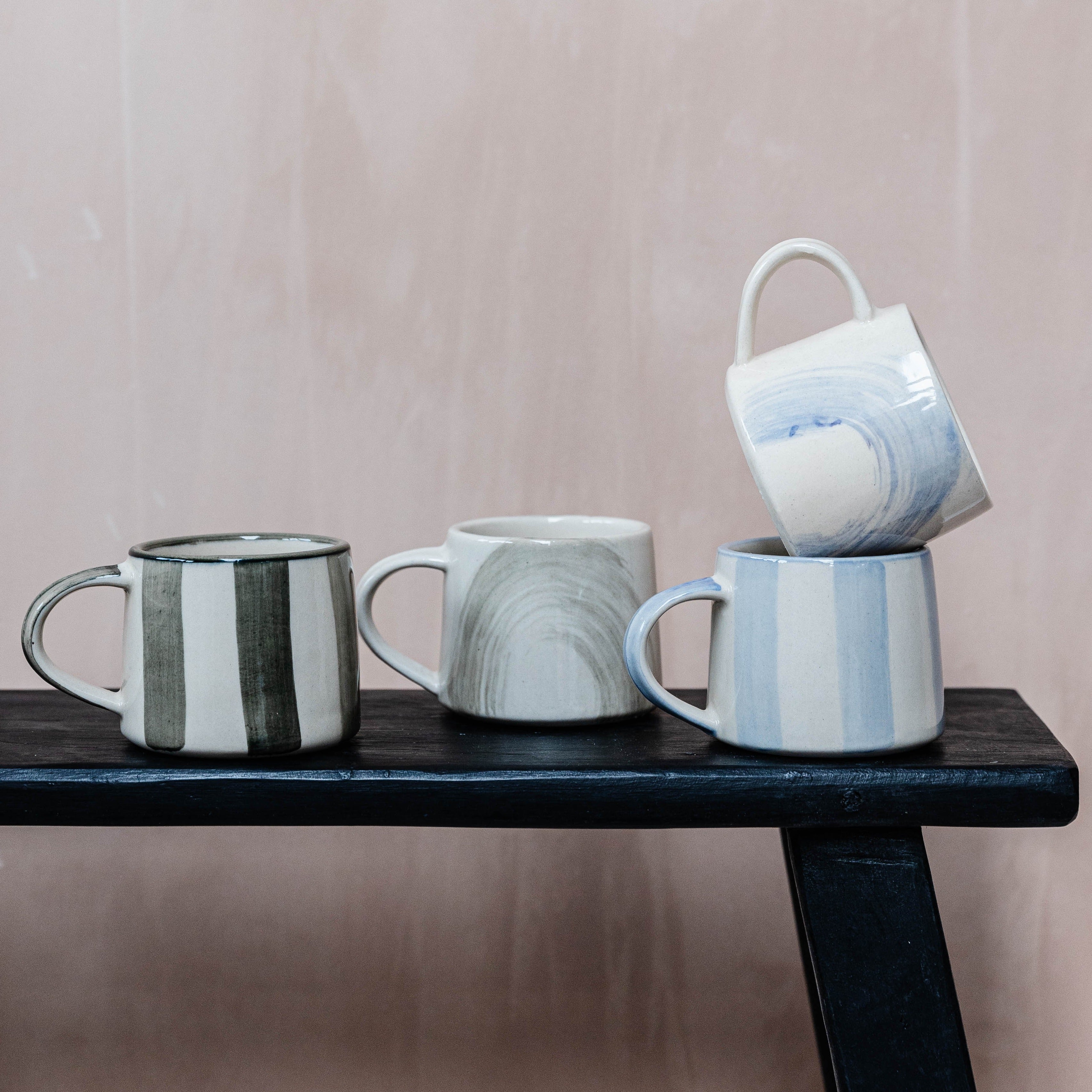 Three hand-painted ceramic mugs stacked on a dark wooden surface.