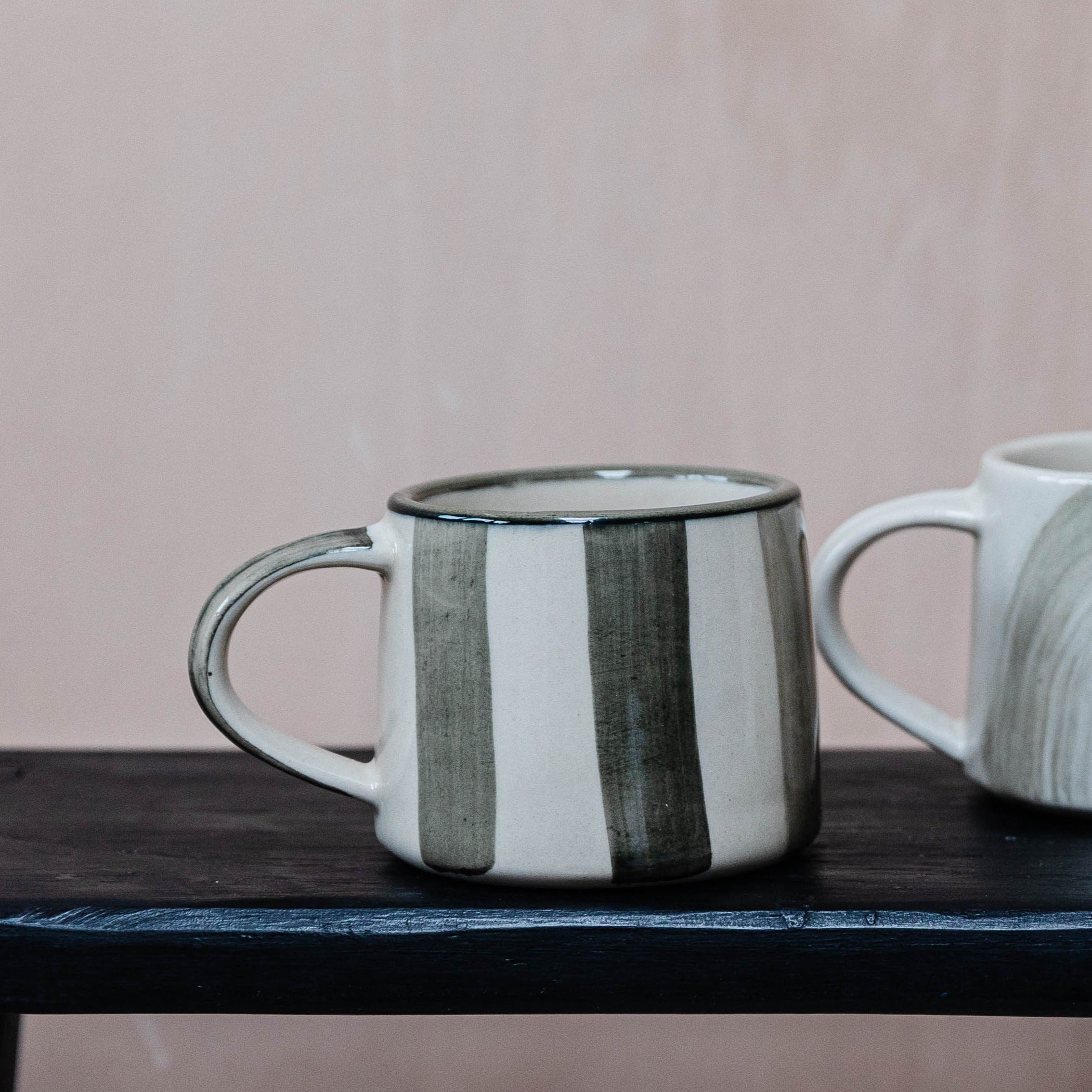 Cream-colored mug with vertical dark gray stripes, featuring a sturdy handle.