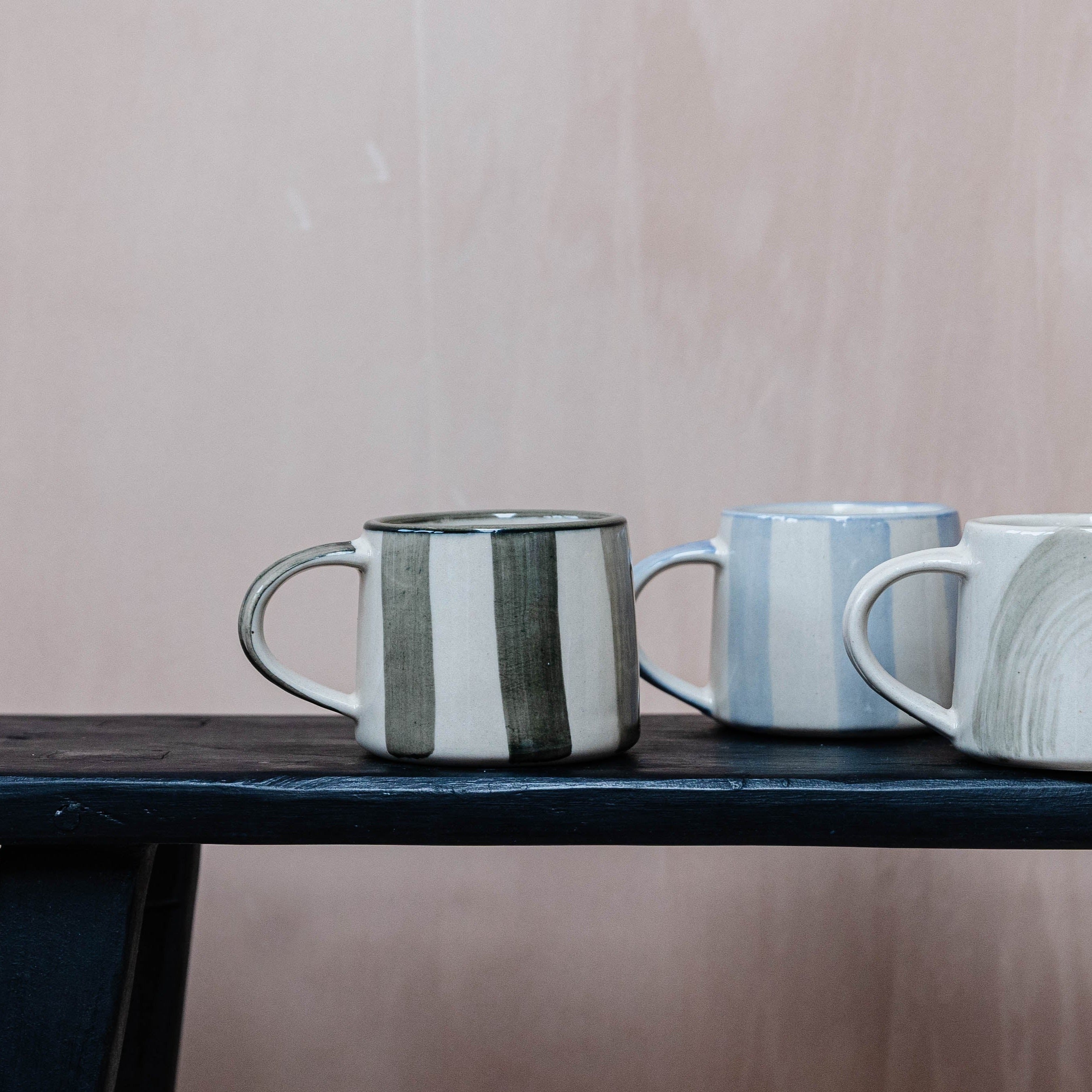 Three ceramic mugs with vertical stripes; one mug features dark green stripes, others have light blue and muted green