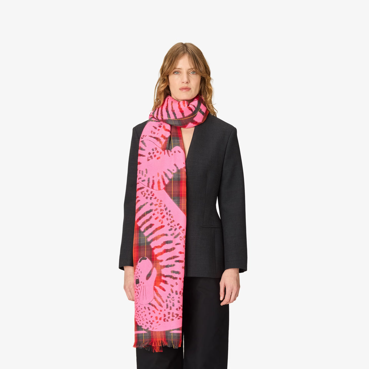 A model wearing a black blazer and black trousers, styled with a vibrant pink and red patterned scarf featuring a tiger and leopard print.