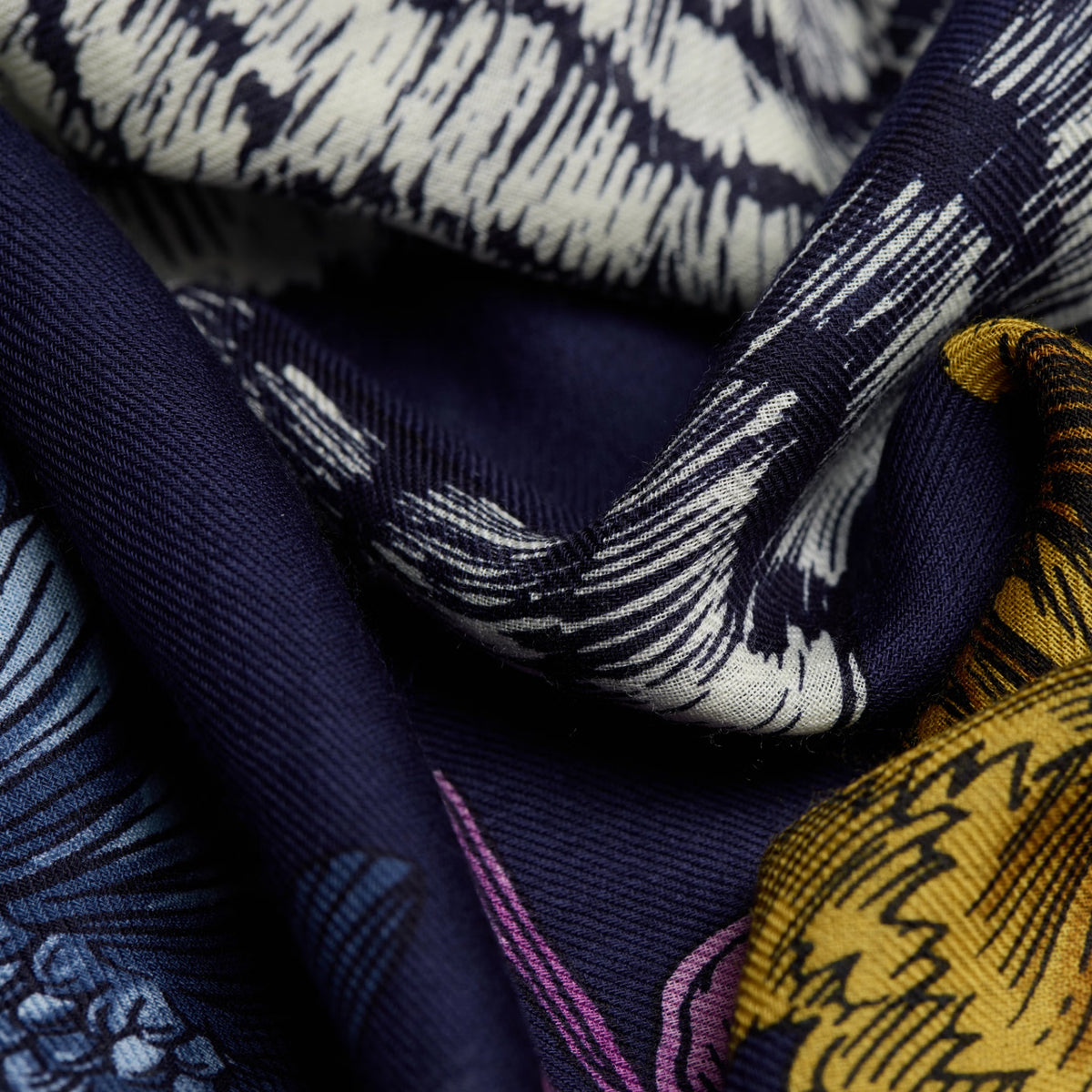 A close-up of a patterned scarf or fabric with navy blue, cream, yellow, and purple woven motifs.
