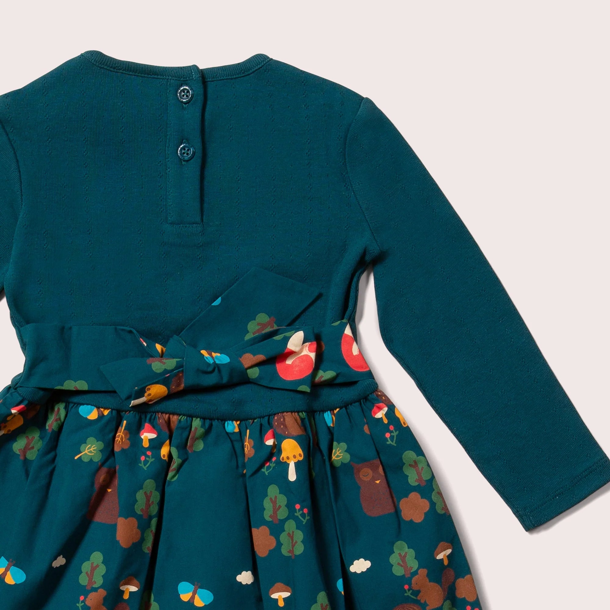 Teal long-sleeved girl's dress with a forest animal print skirt and textured bodice.  Features a self-tie belt.