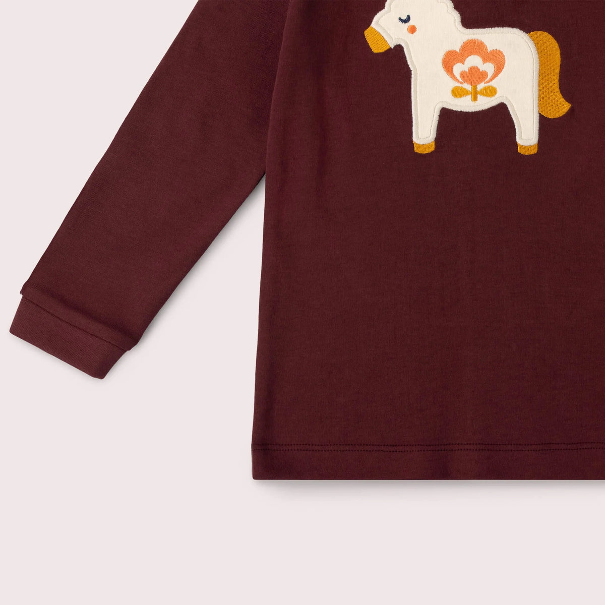 A close-up of a long-sleeve burgundy children's sweatshirt featuring a white embroidered Dala horse with orange and yellow details on the chest, set against a light beige background.