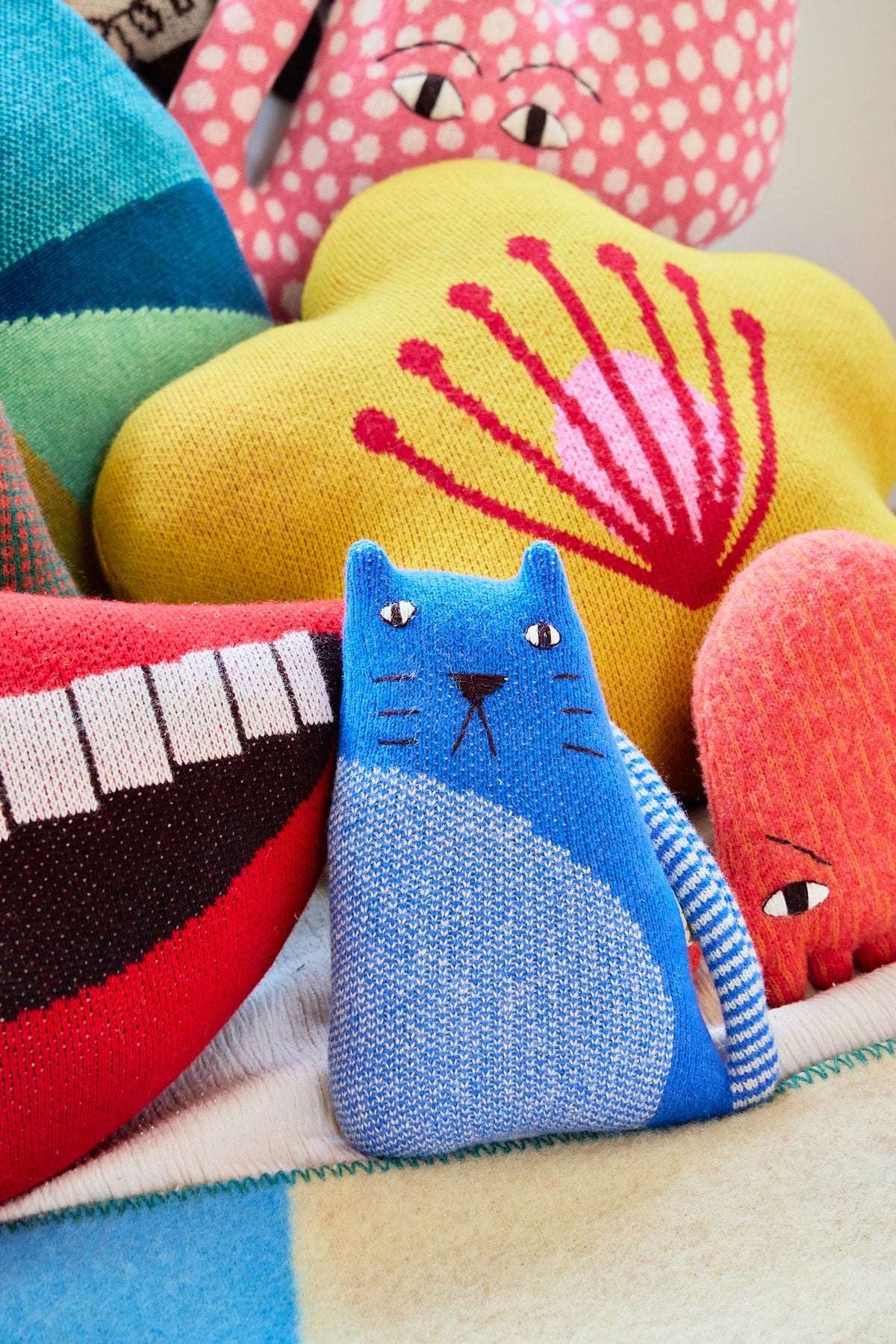 Colorful plush toys including a blue cat, red heart, and yellow shell on a textured surface.