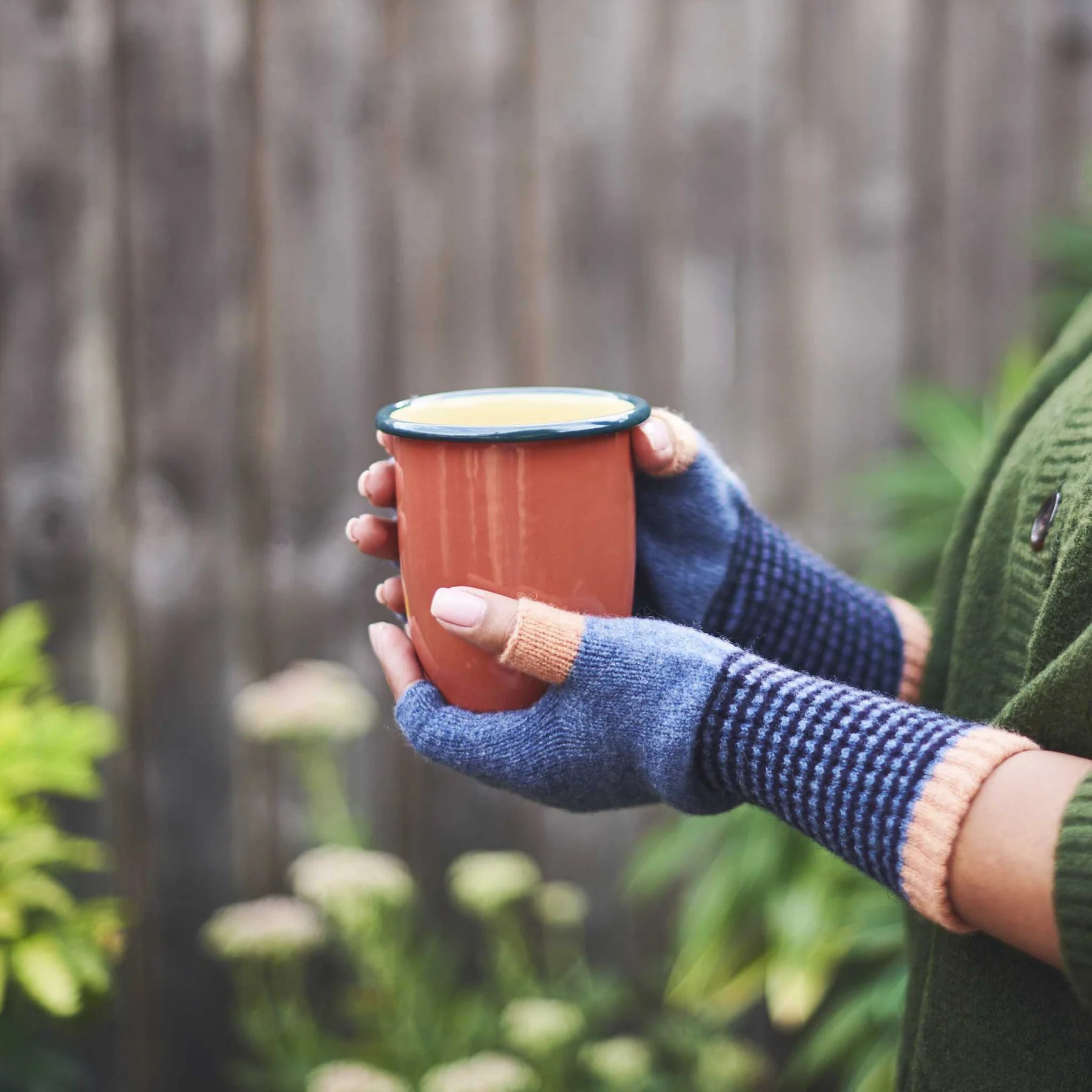 Person holding a terracotta cup with a blurred natural background