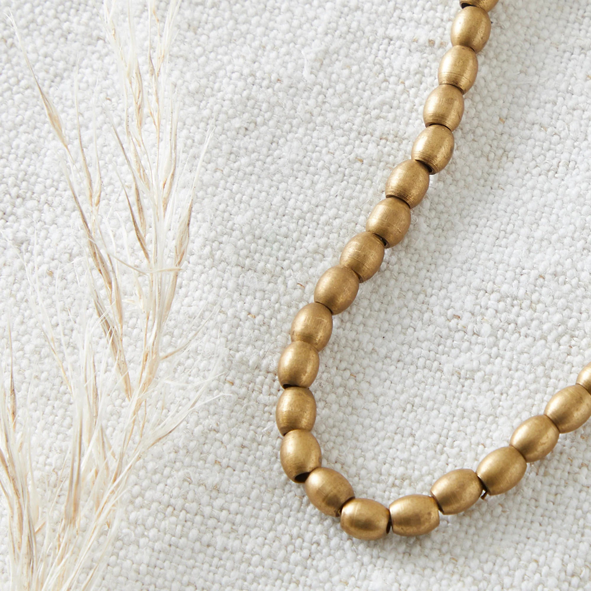 Gold beaded necklace on a textured beige surface with dried grasses.