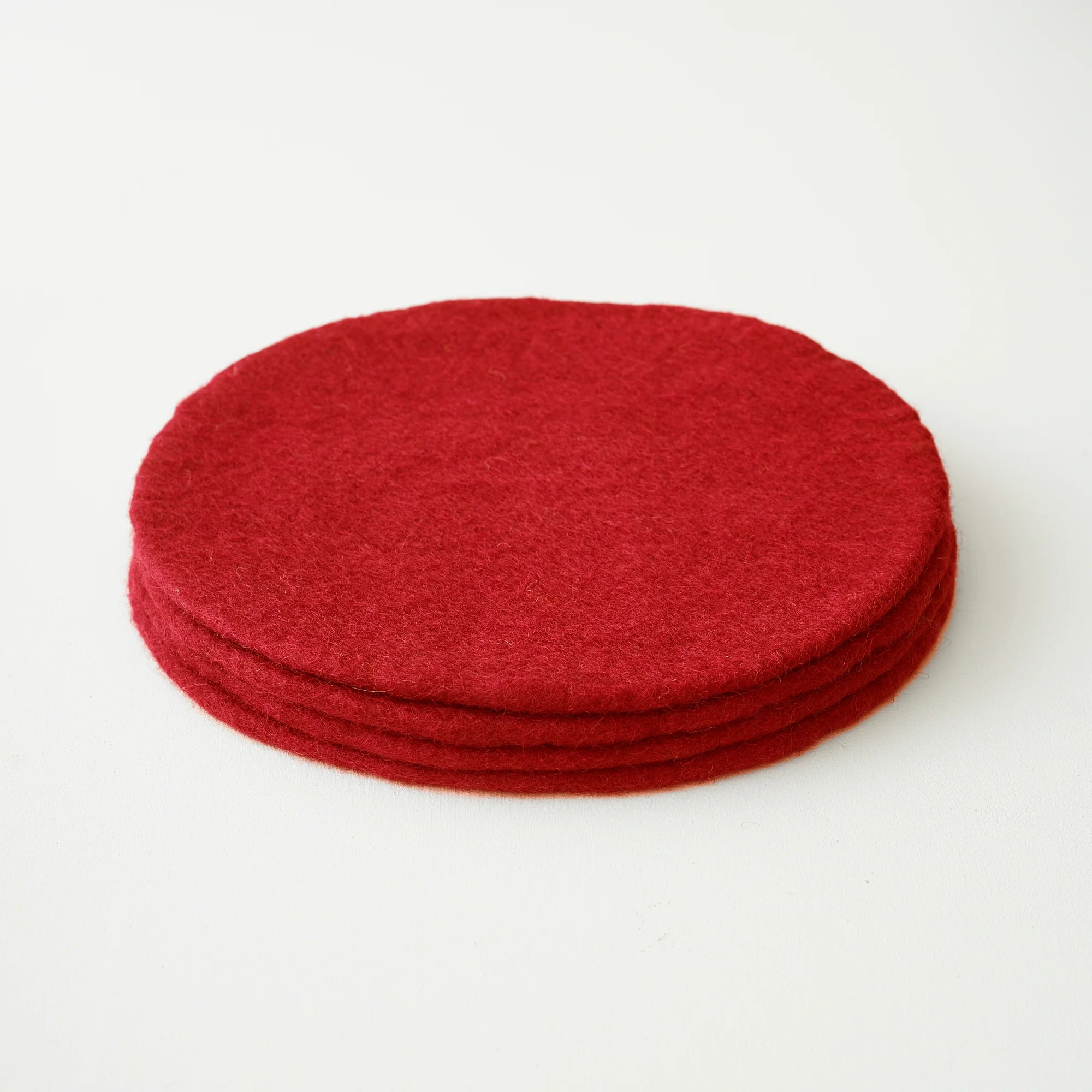 Stack of four dark red round felt coasters.