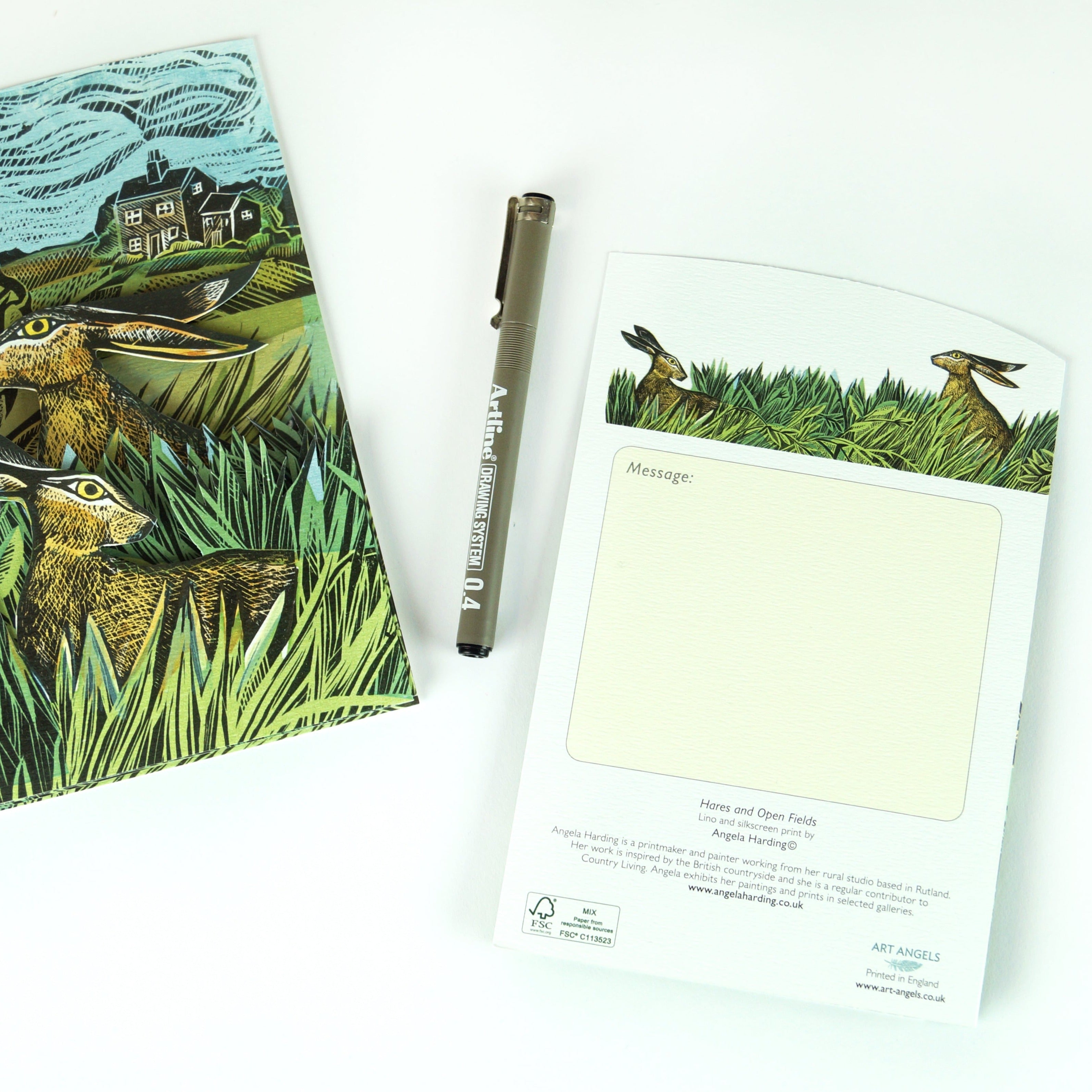 Notecard featuring a linocut print of hares in a field;  space for a message;  includes an Artline 0.4 pen.