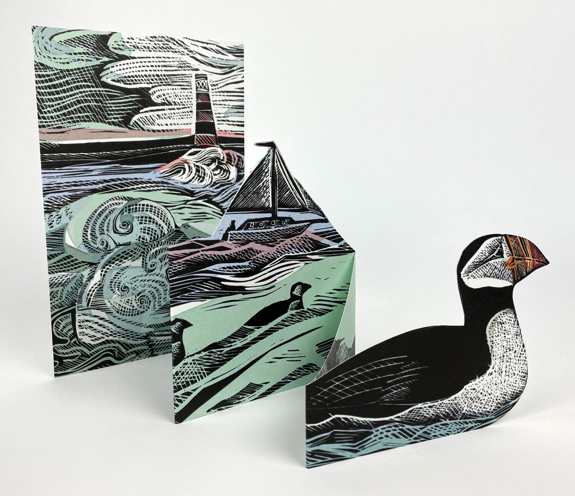 Set of three linocut-style cards featuring a puffin, sailboat, and lighthouse;  black, teal, and white color palette.