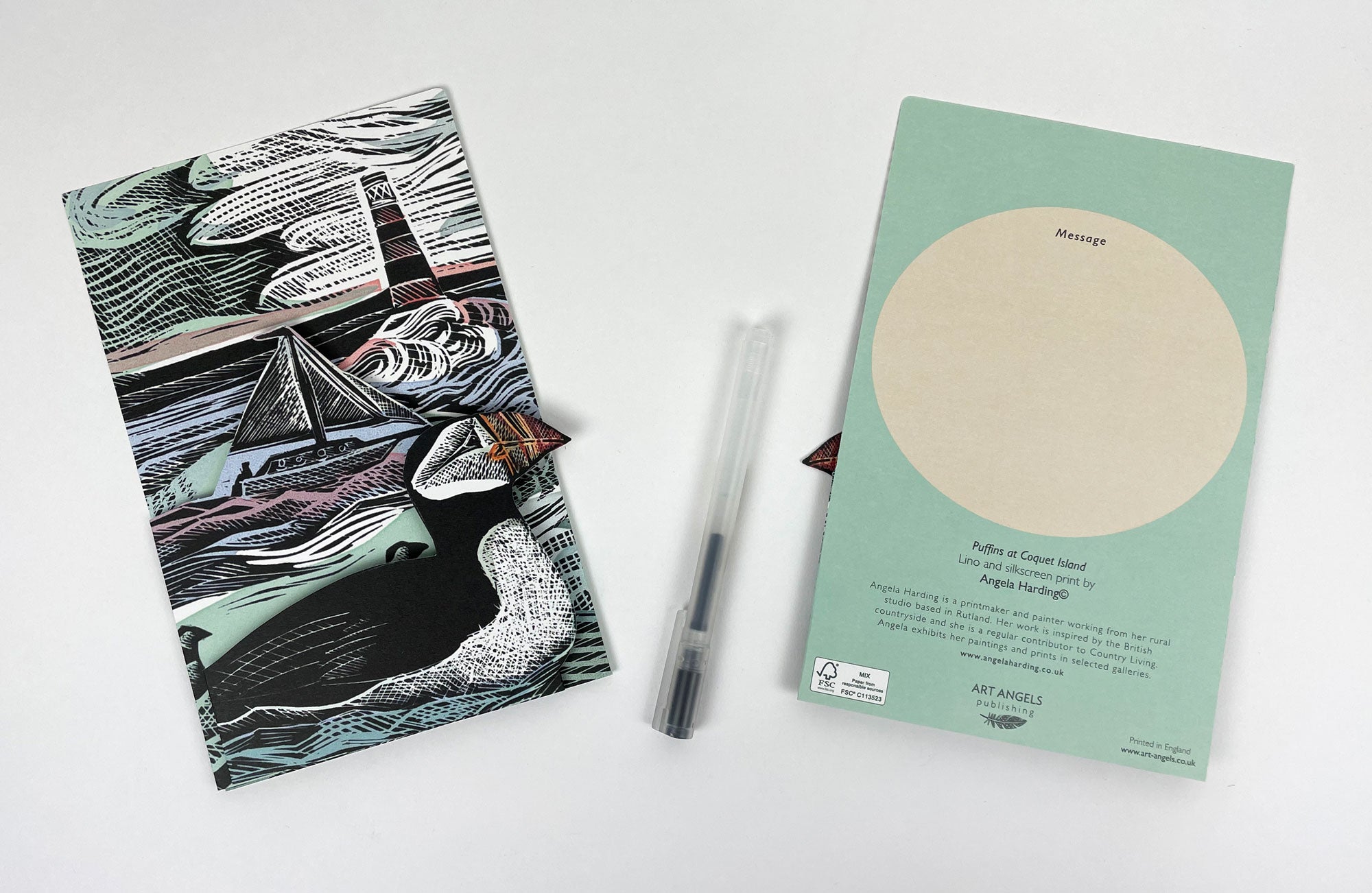 Folded notecard featuring a linocut print of puffins, a sailboat, and a lighthouse at sea.