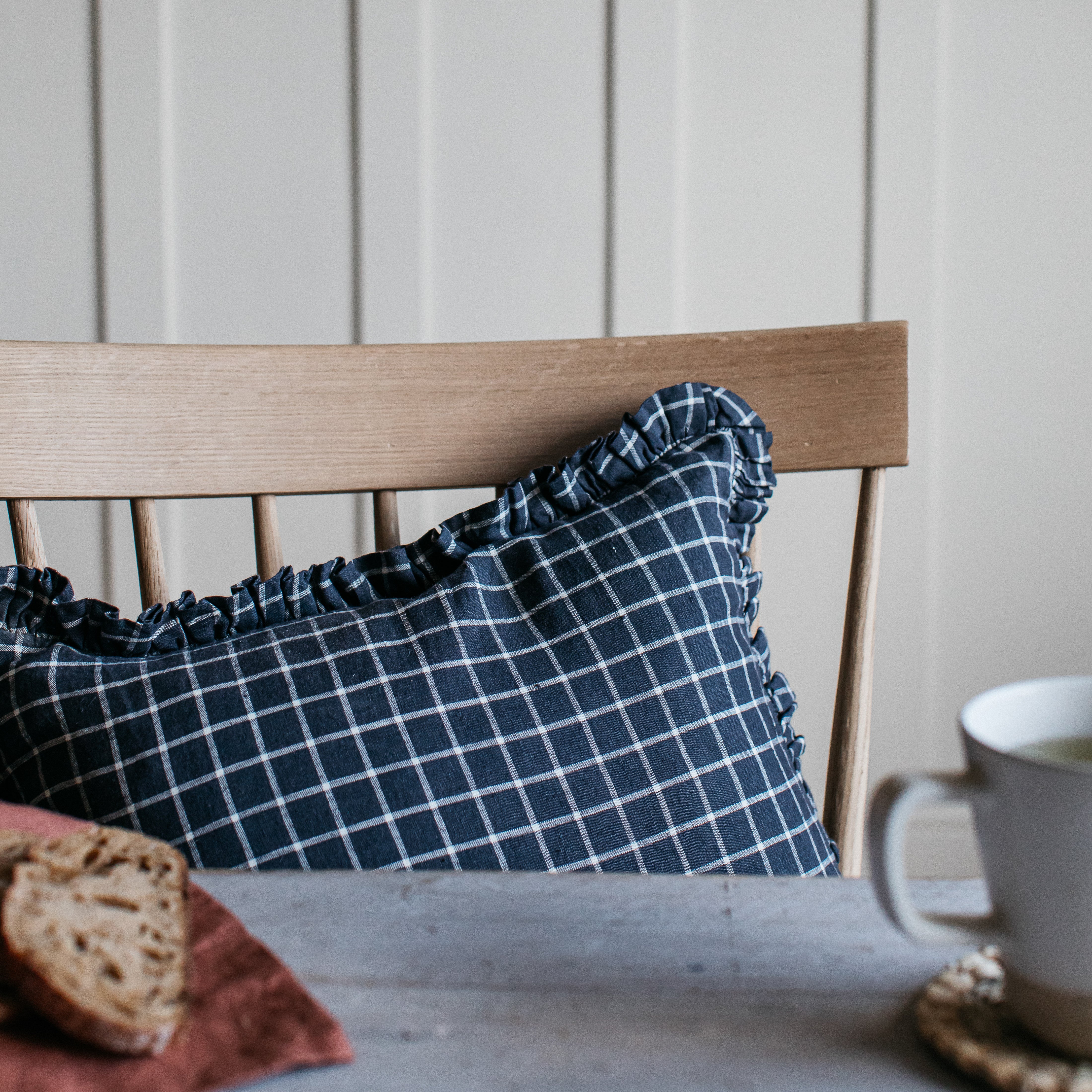 Navy blue and white gingham cushion with ruffled edges, resting on a light wood chair.
