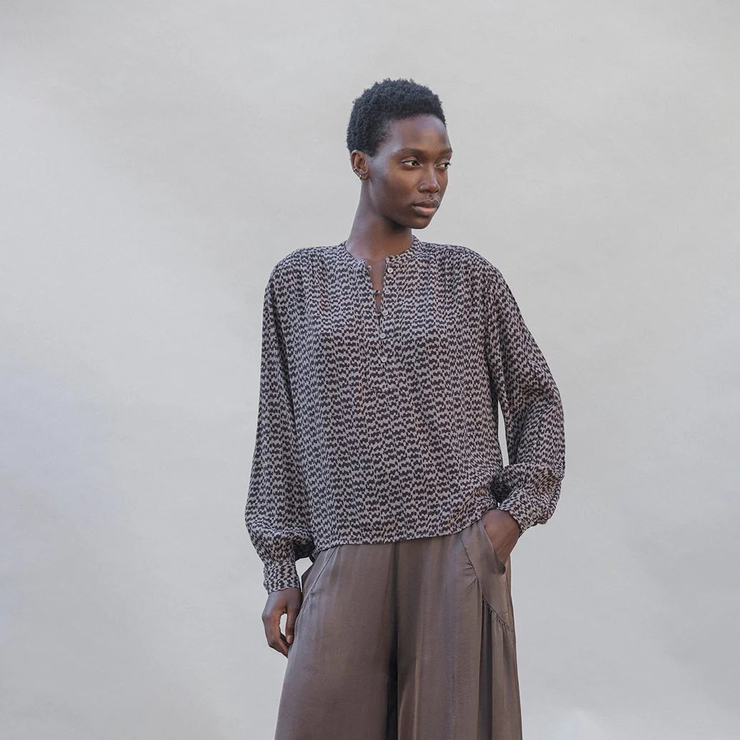 Person wearing a patterned shirt and brown wide-leg pants against a plain background