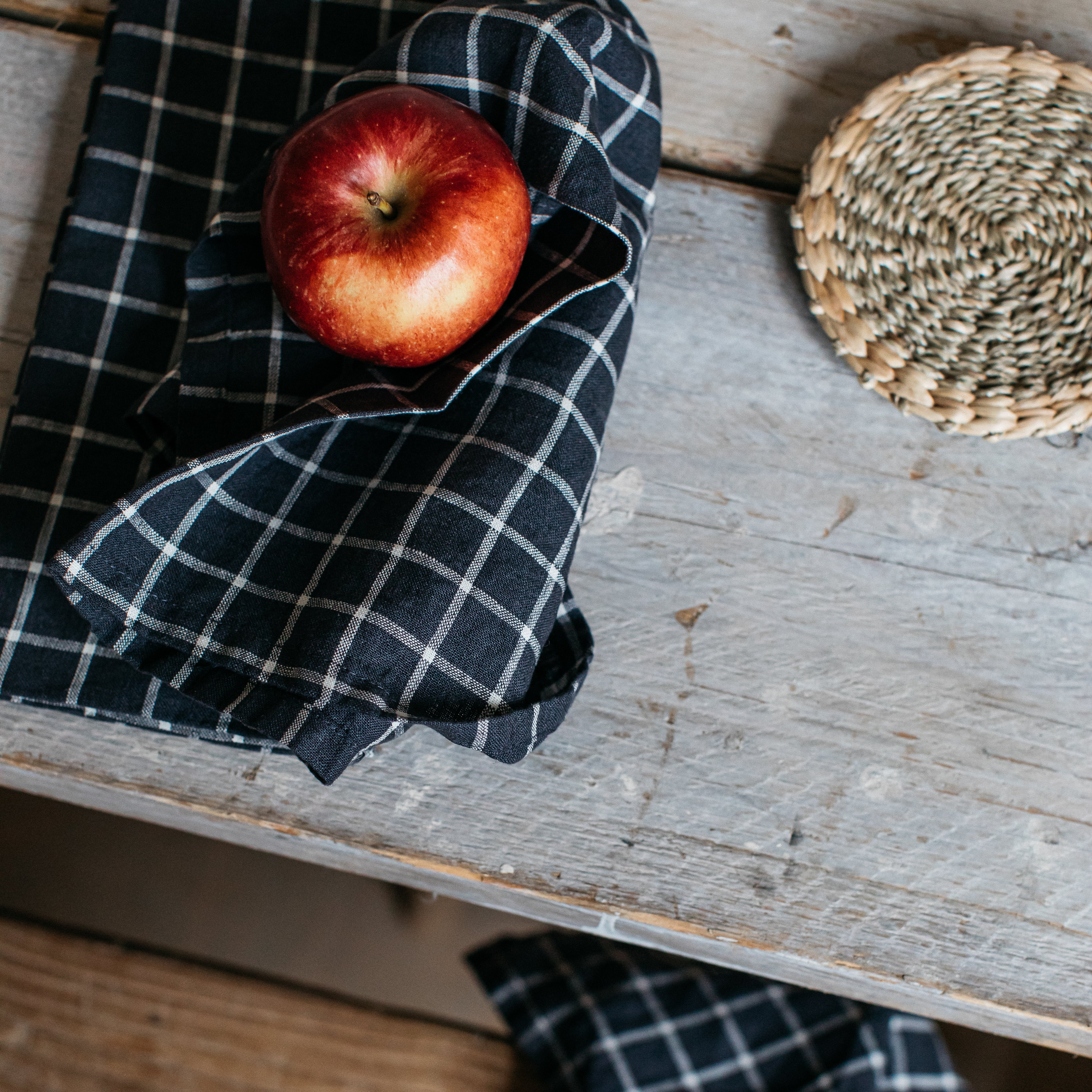 A red apple nestled in a dark navy blue and white gingham tea towel.