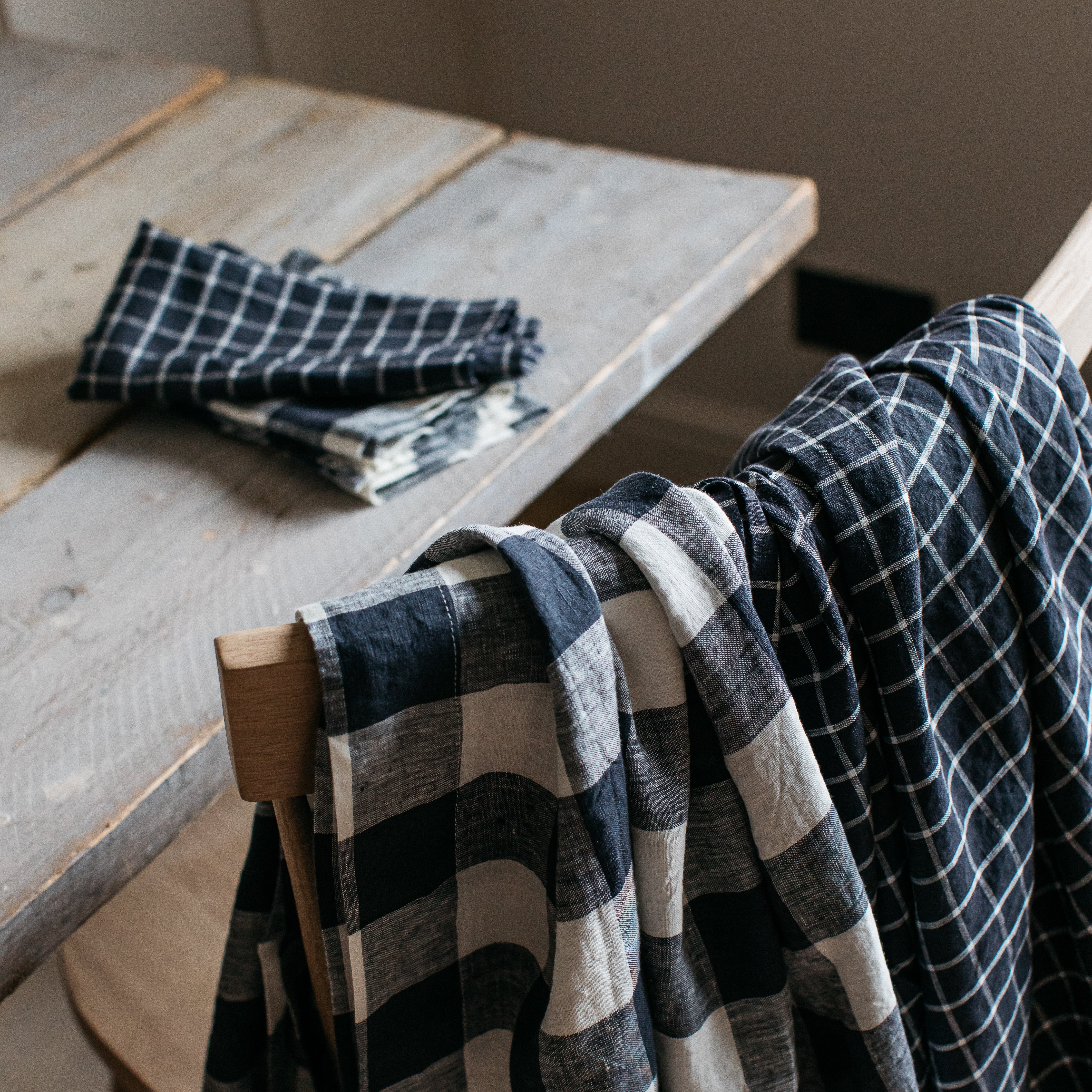 Black and white checkered linen fabric draped over a wooden chair.  A similar folded fabric is on a nearby table.