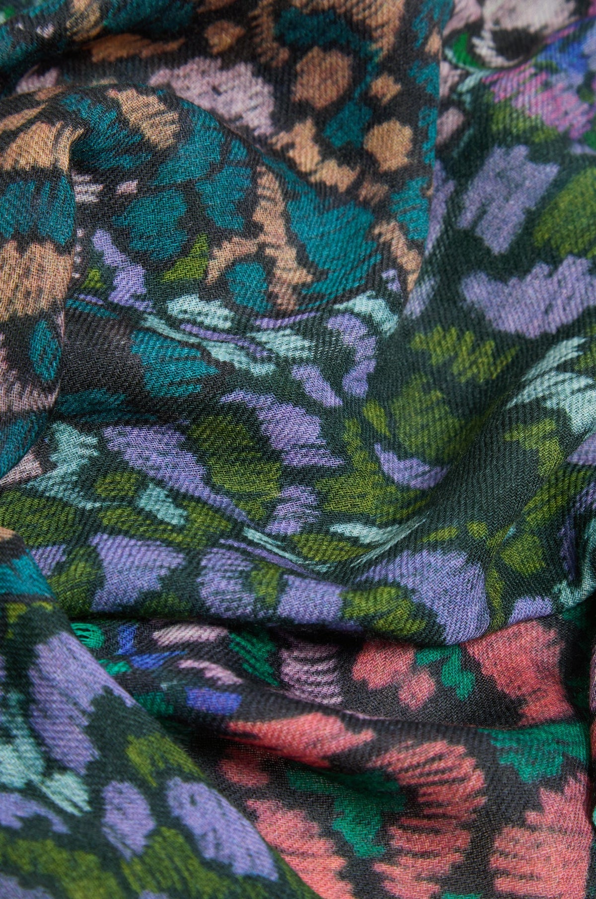 A close-up of a multicolor woven fabric with an abstract floral or leaf-like pattern in teal, green, purple, pink, and brown on a dark background.