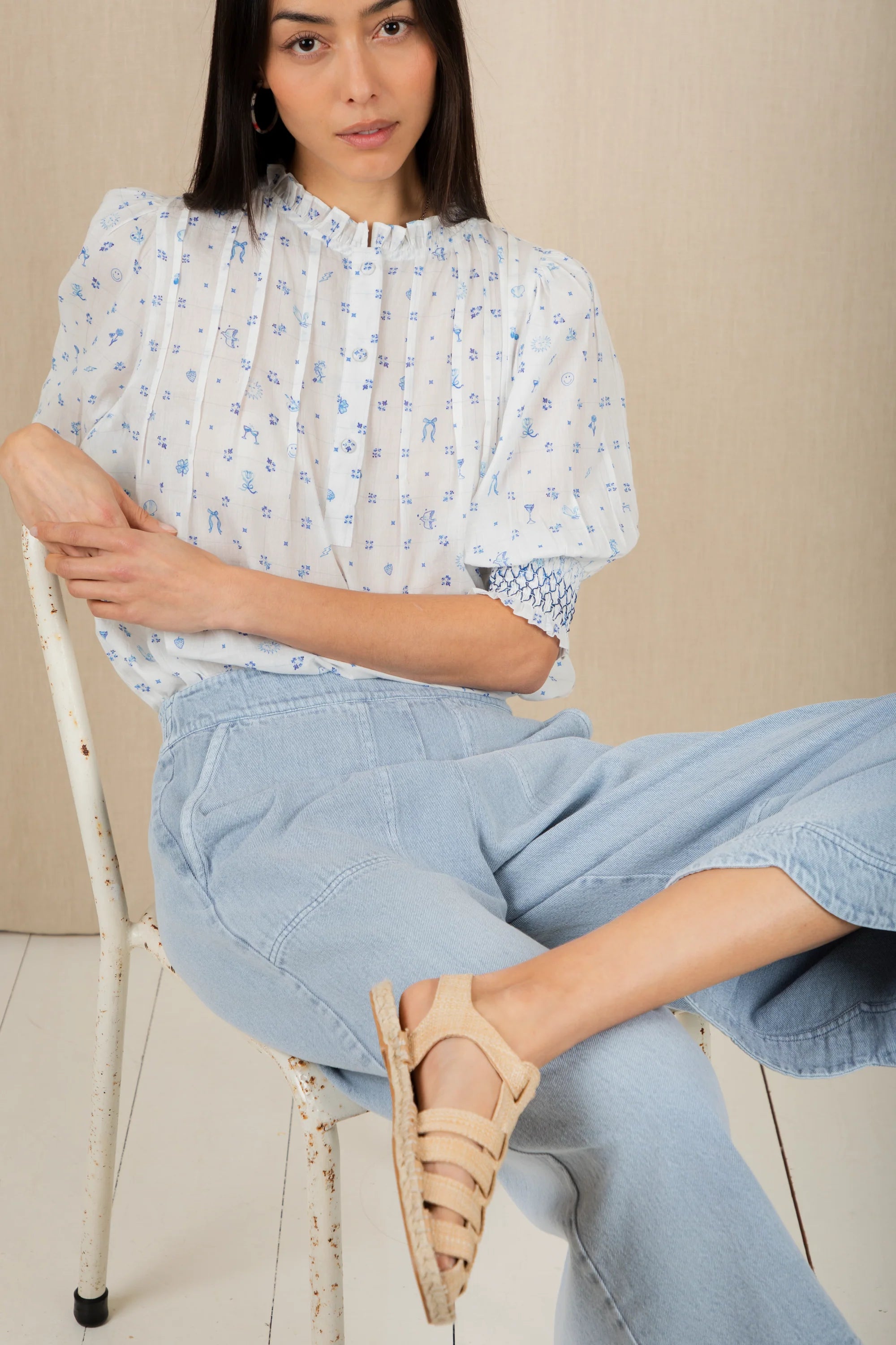 Woman sitting on a chair wearing a light blue patterned blouse and light blue jeans.
