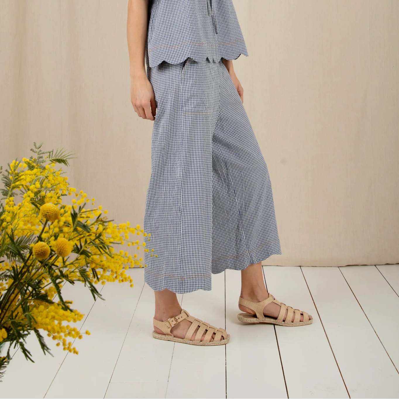 Woman wearing a light blue outfit standing next to a yellow flower arrangement on a wooden floor.