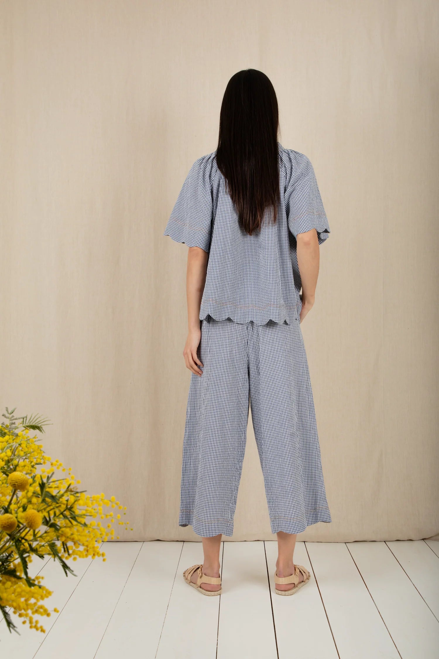 Woman wearing a light blue outfit standing in front of a beige wall with a white floor.