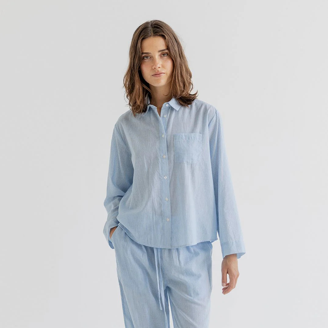Woman wearing a light blue pajama set with lace details on a white background