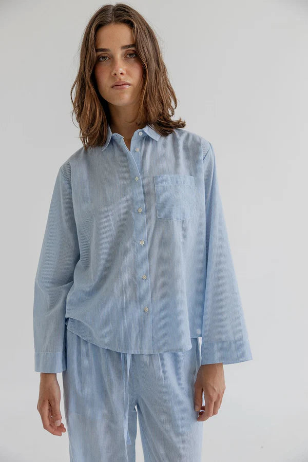 Person wearing a light blue shirt and pants on a plain background