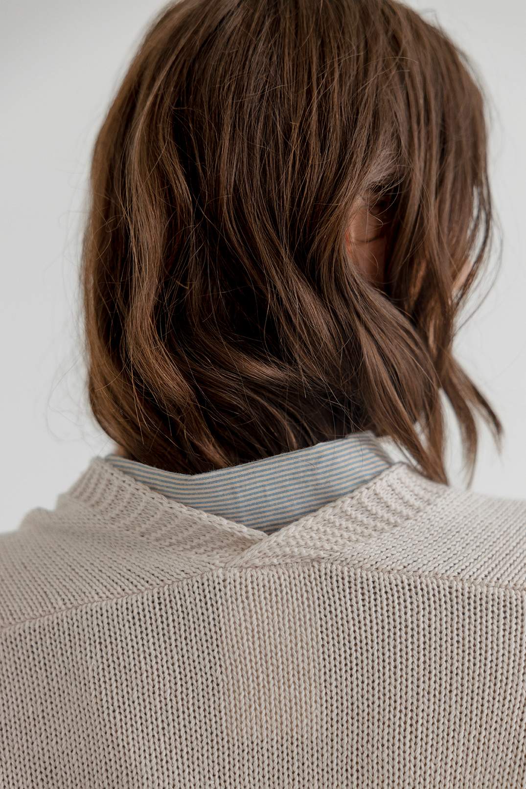 Person wearing a beige knitted sweater with a neutral background