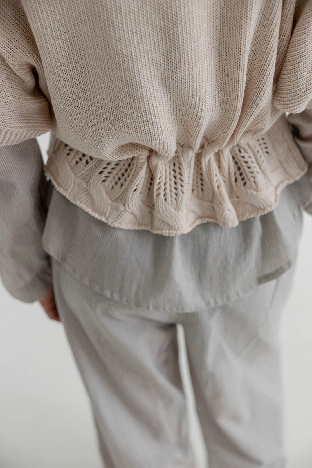 Close-up of a person wearing a beige knit top and light gray pants on a plain background