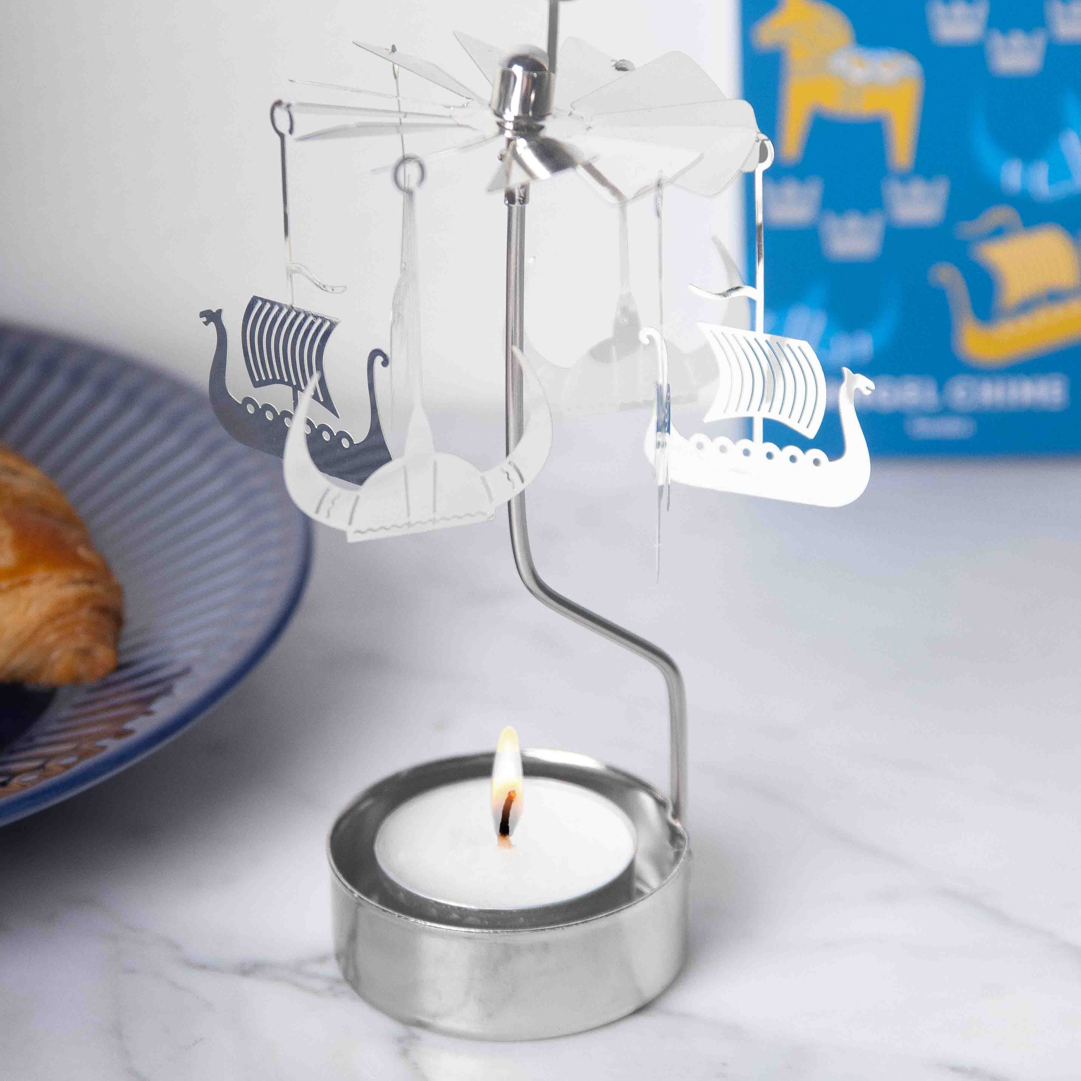 Silver metal candleholder with a rotating carousel featuring cutout Viking ships.  A lit tea light candle sits below.