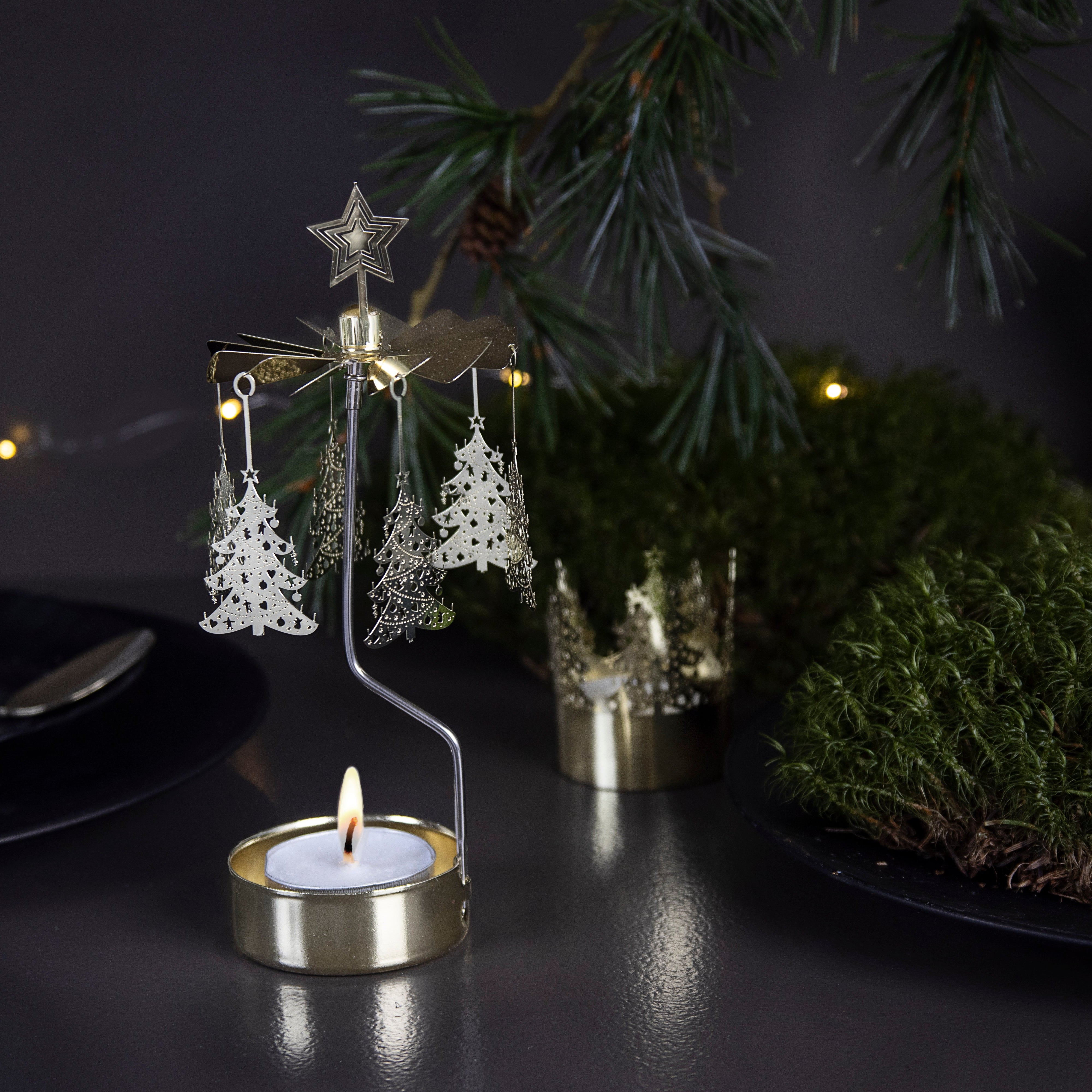 Gold metal candleholder with a lit tea light and rotating Christmas tree cutouts.