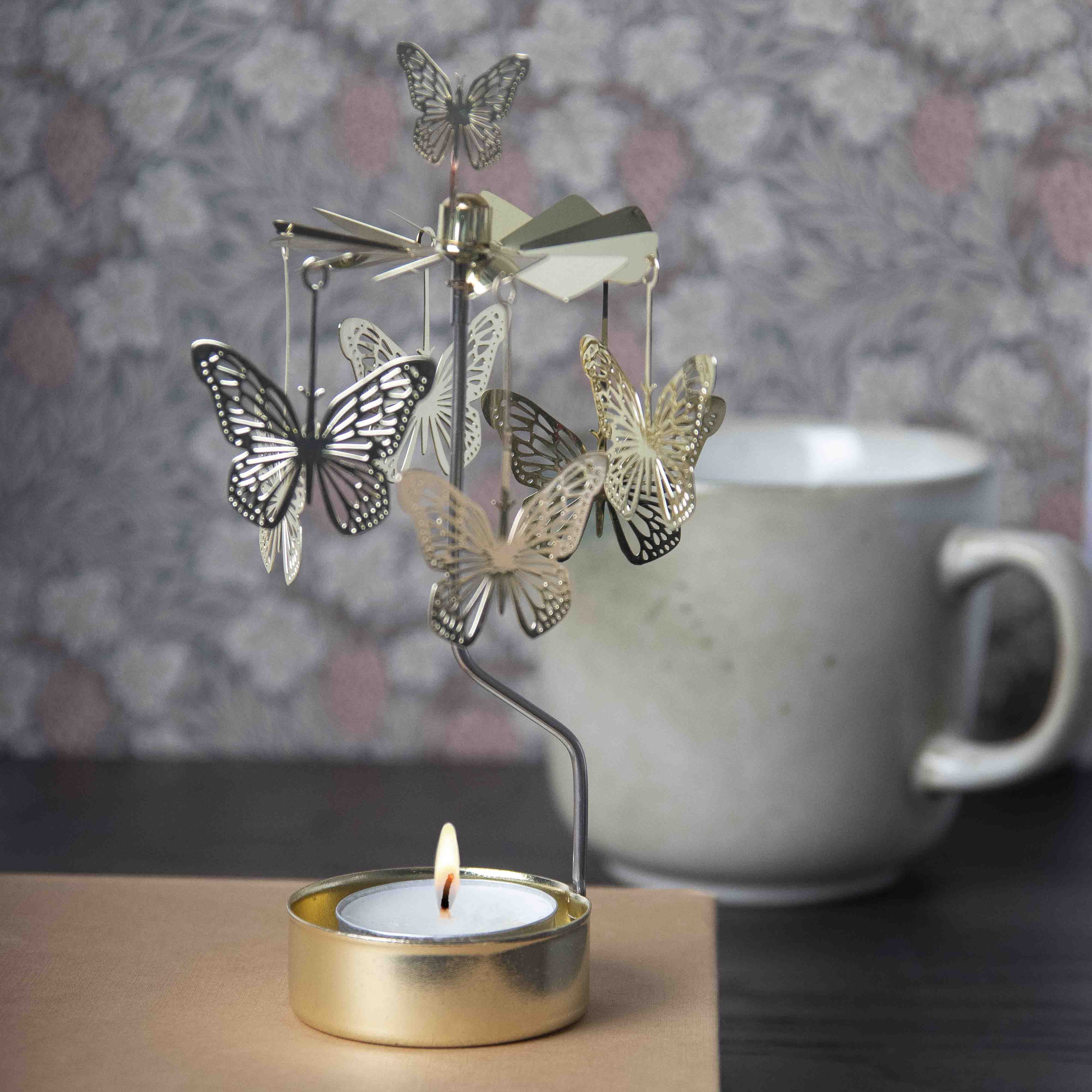 Butterfly-shaped metal decoration with a lit tealight candle on a wooden surface.