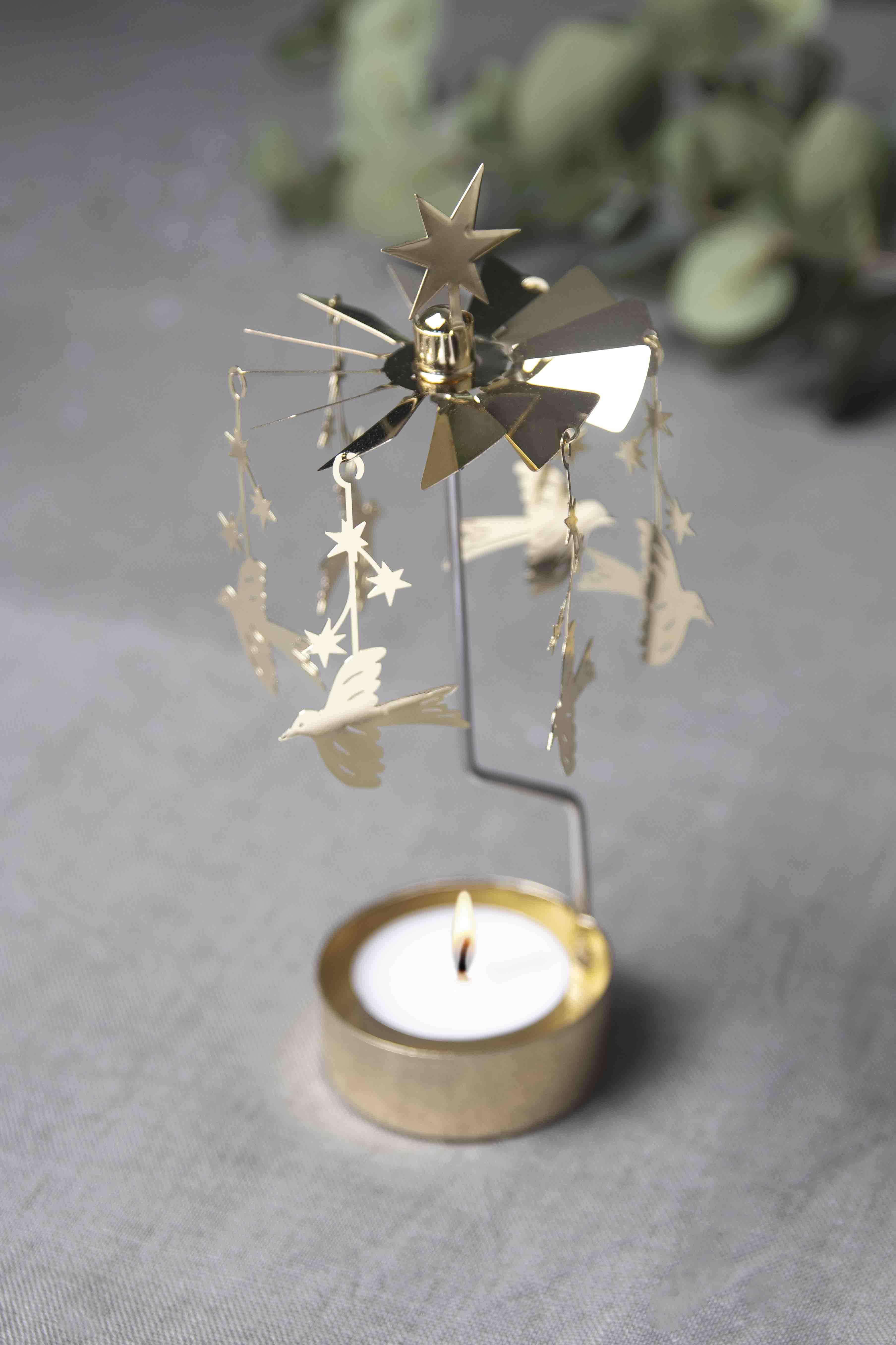 Decorative metal candle holder with stars and birds on a gray surface.