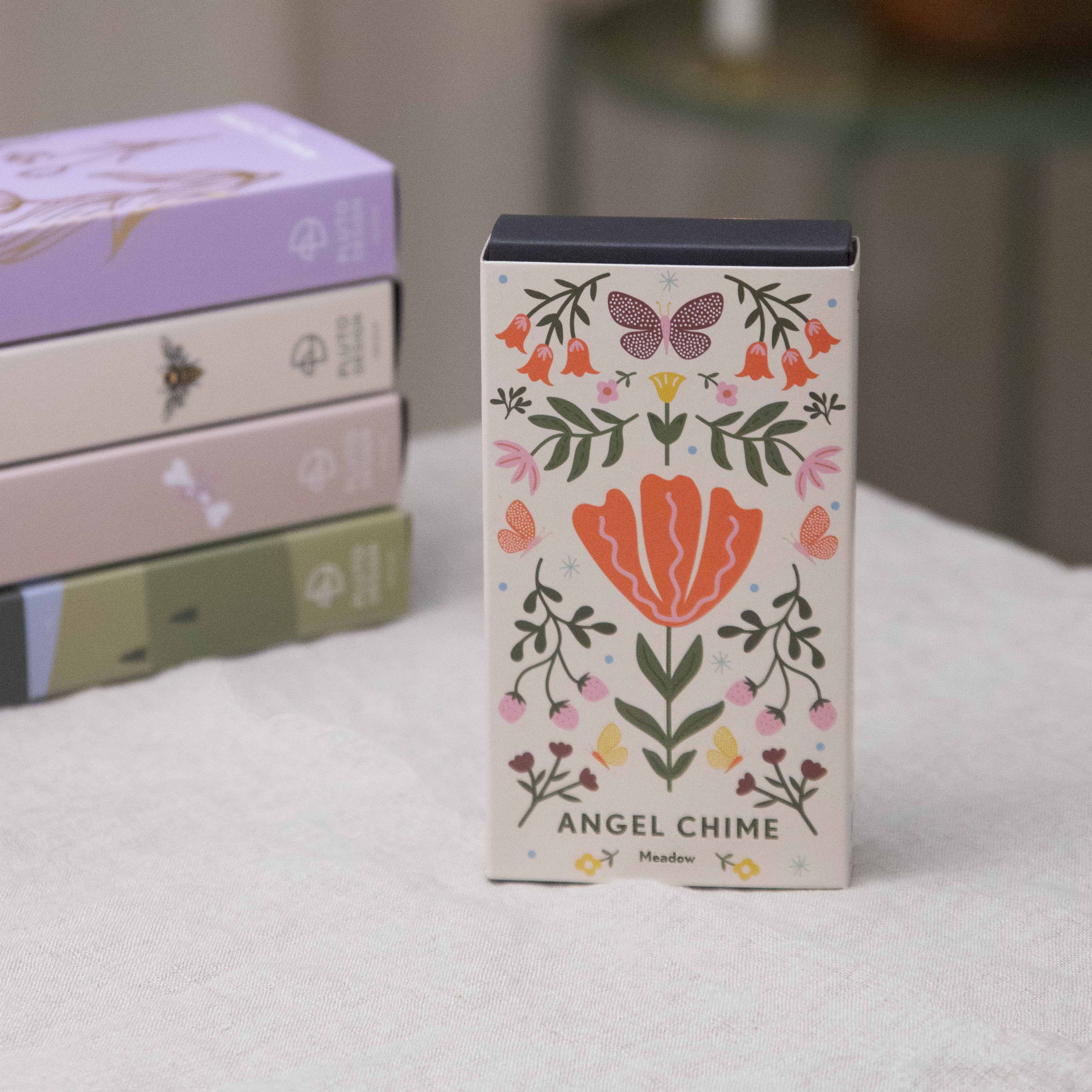 Decorative box with floral design and 'Angel Chime' text on a surface with books and a candle in the background.